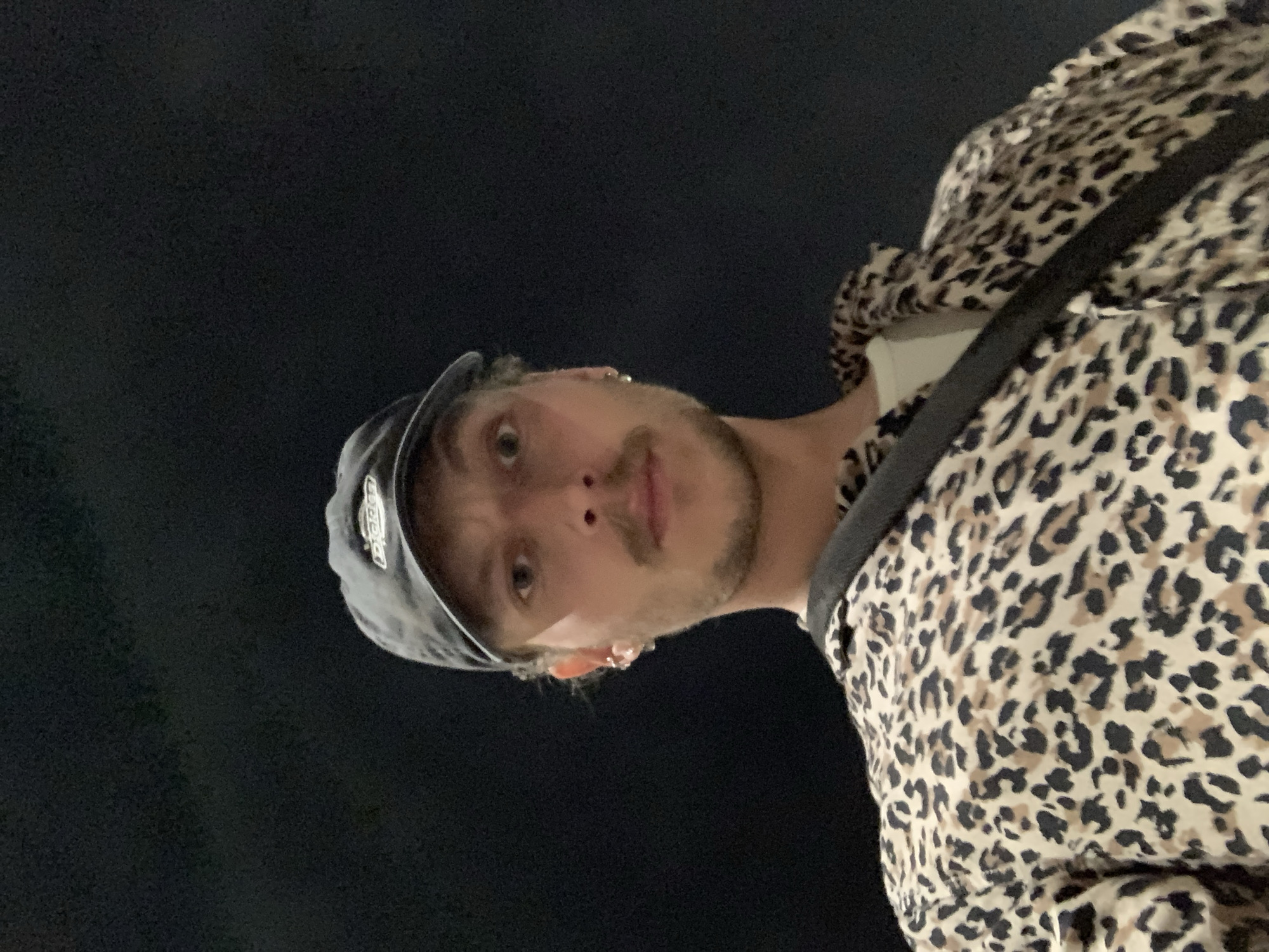A selfie captured at night shows a person wearing a hat and a leopard-print jacket. The background appears to be dark and indistinct. There is no information in the image that allows identification of the specific location as Tel-Aviv, Israel, or any other city.