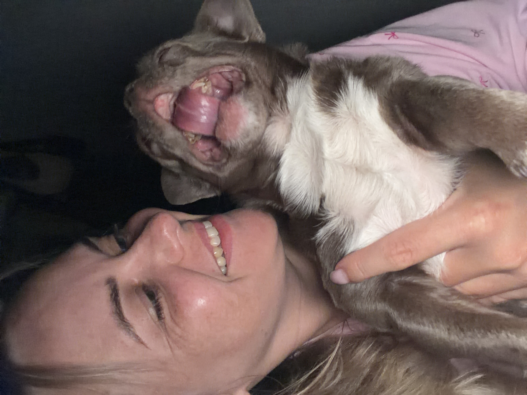 The image shows a woman holding a puppy. The woman has blonde hair and is smiling. The puppy is brown and white and appears to be yawning or crying out. The background is dark. There is no information about the location in Votkinsk, Russia.