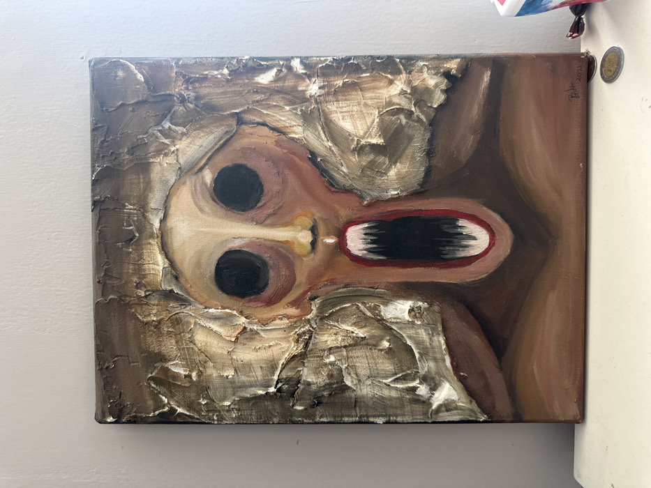 A square painting features a stylized face with large, black, pupil-less eyes and a wide, open mouth showing a dark interior. The face is off-white and brown, surrounded by a heavily textured, beige and brown background. The impasto technique is prominent in the background, creating a rough, three-dimensional effect. The style is somewhat surreal and unsettling, with the face's expression ambiguous. The artist's signature is visible in the top right corner.