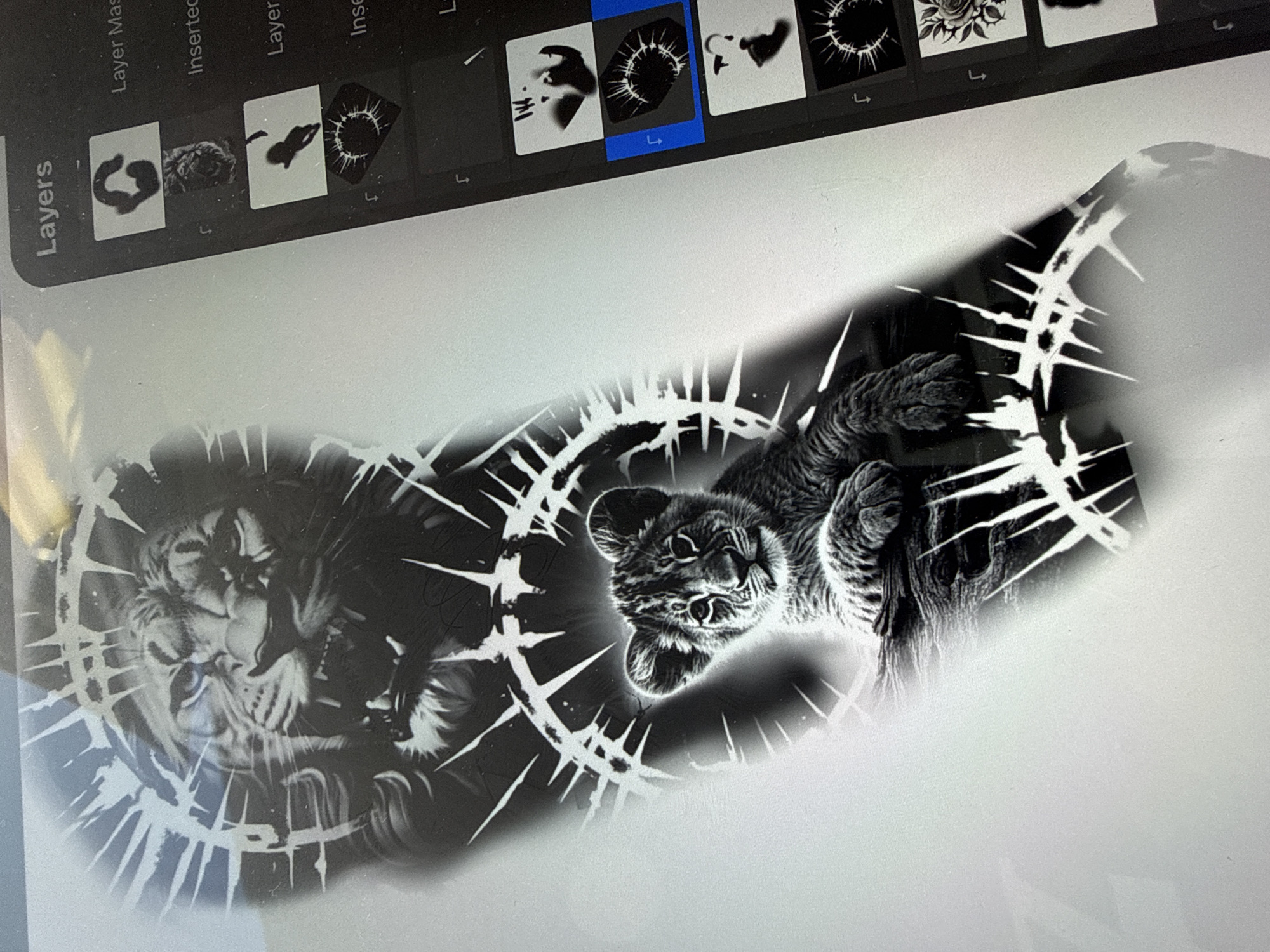A digital art piece on a tablet screen depicts a lion and a lion cub within broken, thorn-like circles. The image is in black and white with grey shading. The lion is on the left, facing forward with visible details of its fur and facial features. The cub is on the right, positioned upside down, with its head oriented towards the viewer. The thorn-like circles surround each animal, creating a fragmented halo effect. The tablet displays a software interface at the top, including layer options and thumbnails, indicating the image is in a stage of digital creation or editing. The setting or location in Sofia, Bulgaria is not evident.