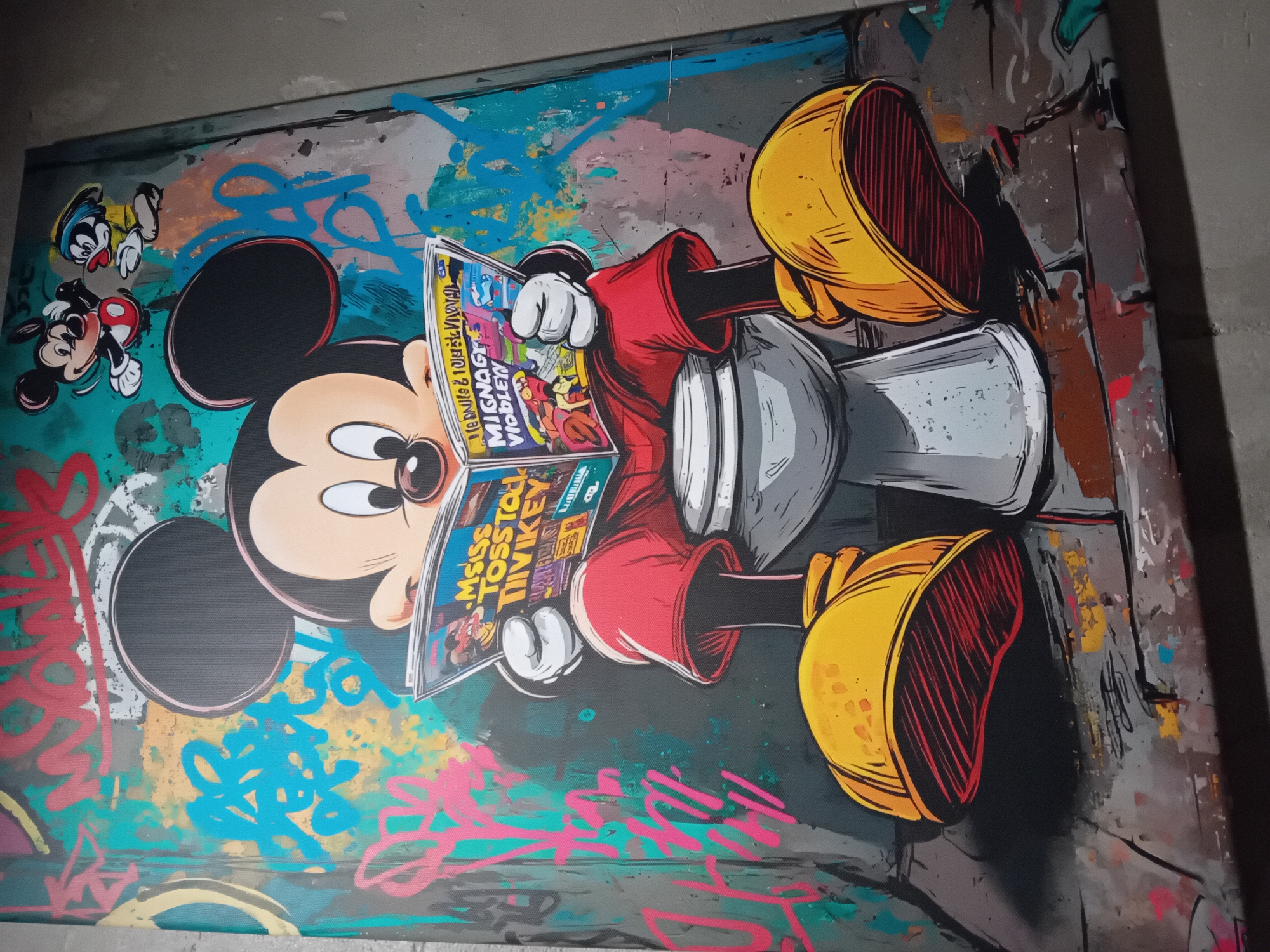 A brightly-colored canvas painting depicts Mickey Mouse sitting and reading a comic book titled "Msiss Tosstoi Mivkey" or a similar iteration. The background of the painting is a mix of colors, including turquoise, pink, blue, and grey, with some graffiti-style elements. Another small Mickey Mouse character is visible in the upper left corner. The painting is likely located in an indoor setting, possibly an art gallery or private home. There is no clear indication to confirm it is in Barcelona, Spain from the image provided.
