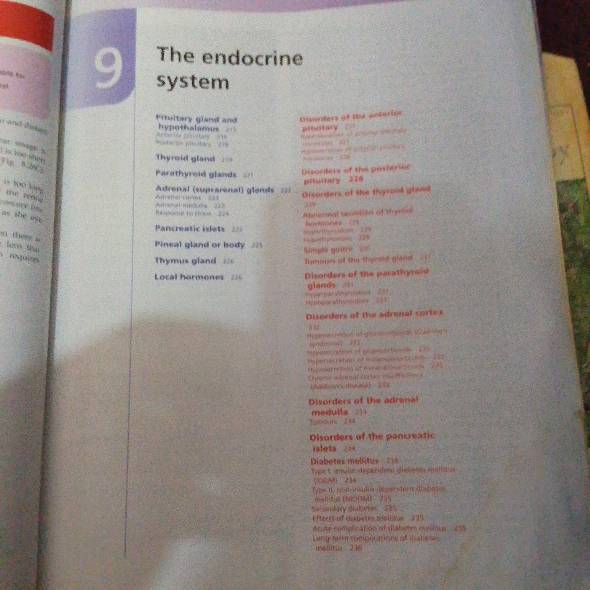 The image is a close-up, high-angle photograph of an open book, likely a textbook, displaying a table of contents or index for a chapter titled "The endocrine system." The chapter number "9" is prominently displayed in a purple box on the left side of the page. The text is organized into main headings with sub-points and corresponding page numbers.
The content visible includes:
* Pituitary gland and hypothalamus
* Thyroid gland
* Parathyroid glands
* Adrenal (suprarenal) glands
* Pancreatic islets
* Pineal gland or body
* Thymus gland
* Local hormones
* Disorders of the anterior pituitary
* Disorders of the posterior pituitary
* Disorders of the thyroid gland (including abnormal secretion of thyroid hormones, simple goitre, and tumours)
* Disorders of the parathyroid glands (including hyperparathyroidism and hypoparathyroidism)
* Disorders of the adrenal cortex (including hypersecretion of glucocorticoids, hyposecretion of glucocorticoids, hypersecretion of mineralocorticoids, and chronic adrenal cortex insufficiency)
* Disorders of the adrenal medulla (including tumours)
* Disorders of the pancreatic islets (including diabetes mellitus, type 1 and type 2 diabetes, secondary diabetes, effects of diabetes mellitus, and long-term complications of diabetes mellitus)
The book appears to be well-lit, with the text being sharp and legible. The background of the image is a blurred mixture of textures and colors, suggesting the book is placed on a surface or in a general environment.
There is no information in the image that can be used to determine its location in Jalingo, Nigeria, or any other geographical location. The image solely depicts the content of a book.