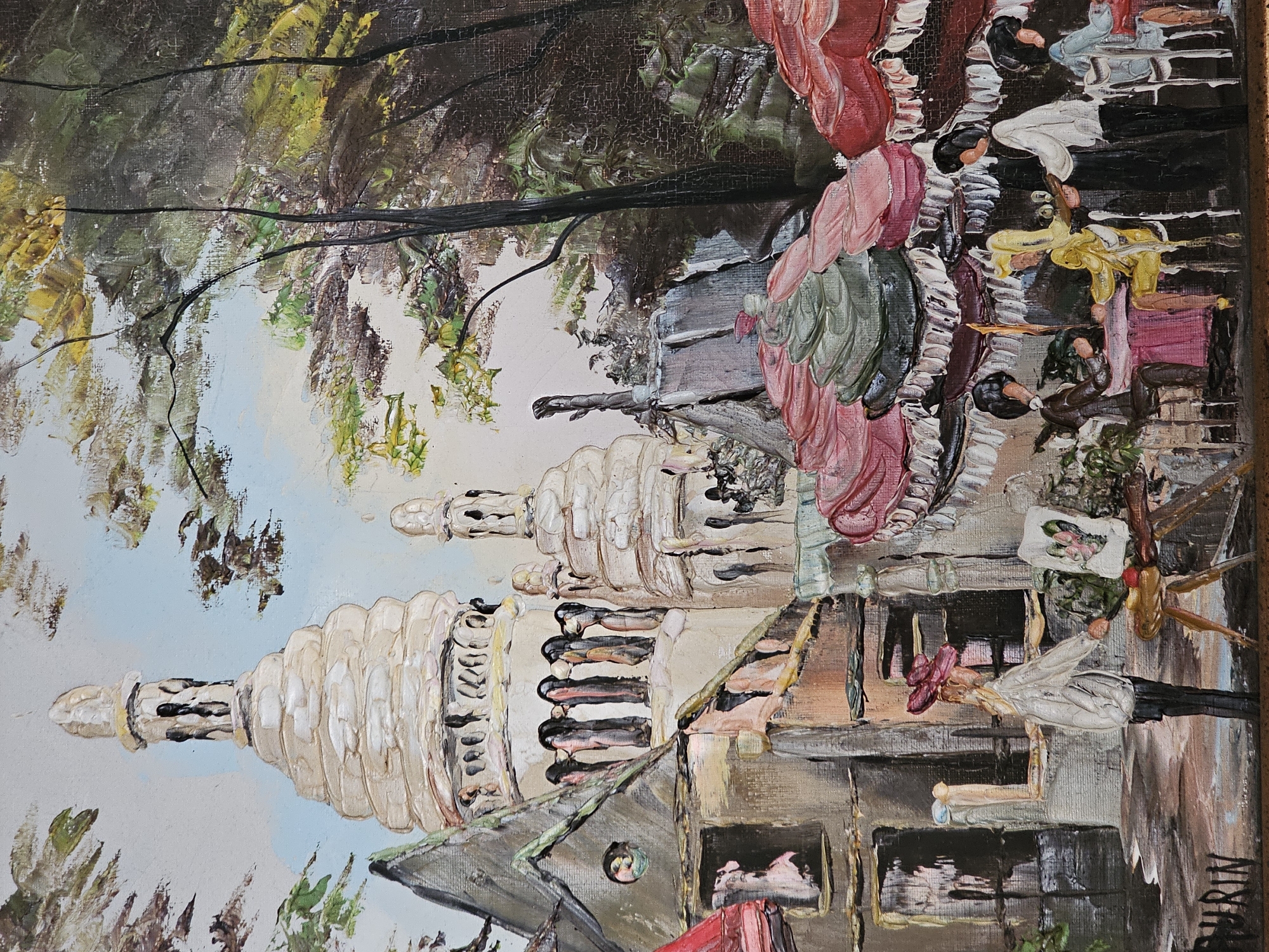 The oil painting depicts a Parisian street scene with a prominent church structure resembling Sacré-Cœur Basilica in Montmartre, Paris, France. In the foreground, an artist is shown painting at an easel, with a small canvas displaying a heart motif. Several patrons are seated at tables under umbrellas, appearing to be at an outdoor cafe. The style of the painting is impressionistic, characterized by thick brushstrokes and vibrant colors. The image does not depict any location in Amarillo, United States of America.