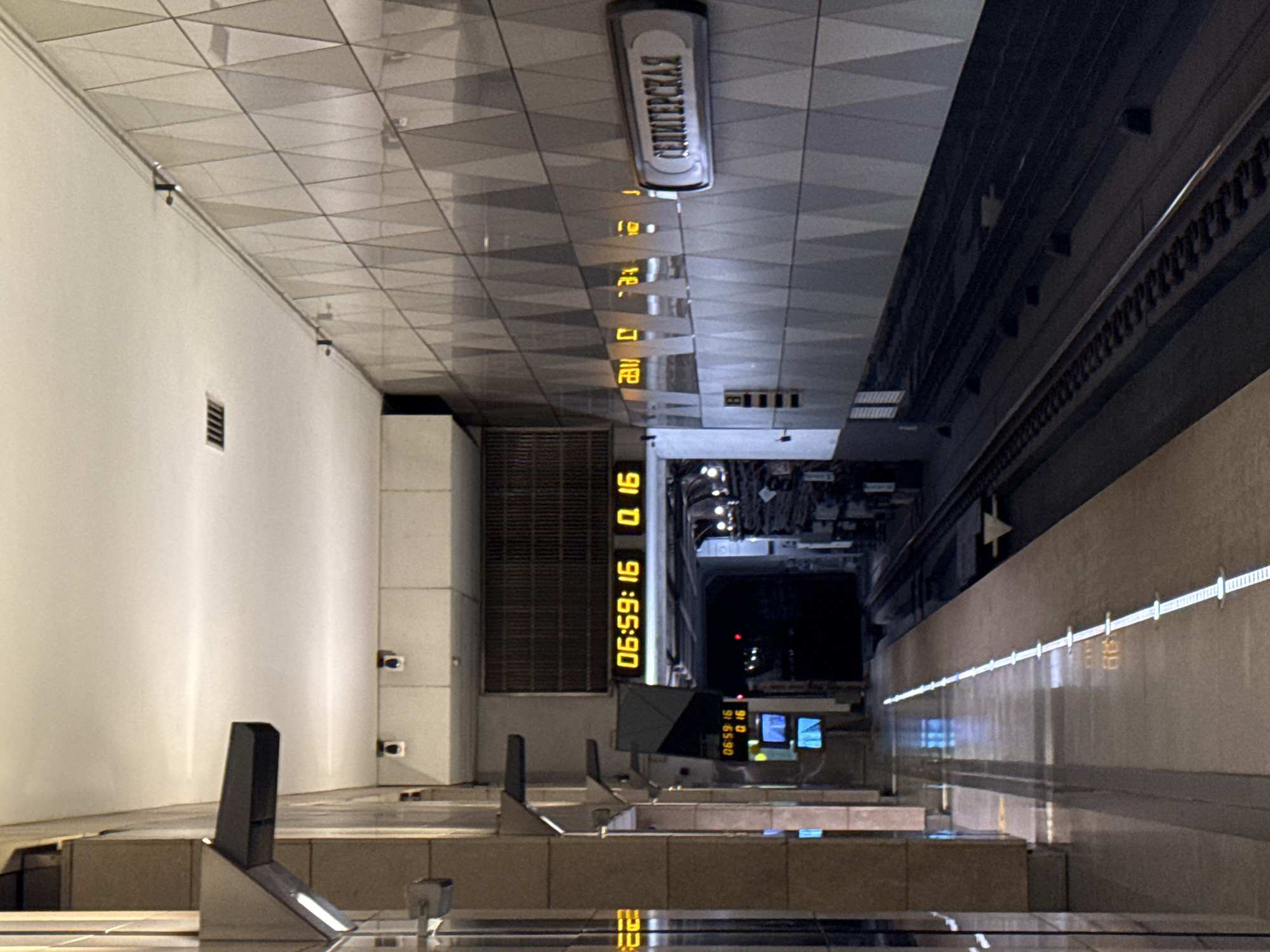 The image shows a subway station platform in Moscow, Russia. The platform is mostly empty, with a few digital signs displaying train times. The walls of the station are decorated with a geometric pattern, and there are lights installed along the ceiling. A train track runs along the platform. The station sign reads "СЕДИМПЕРСКАЯ" (Sedimperskaya), indicating the station's name.
