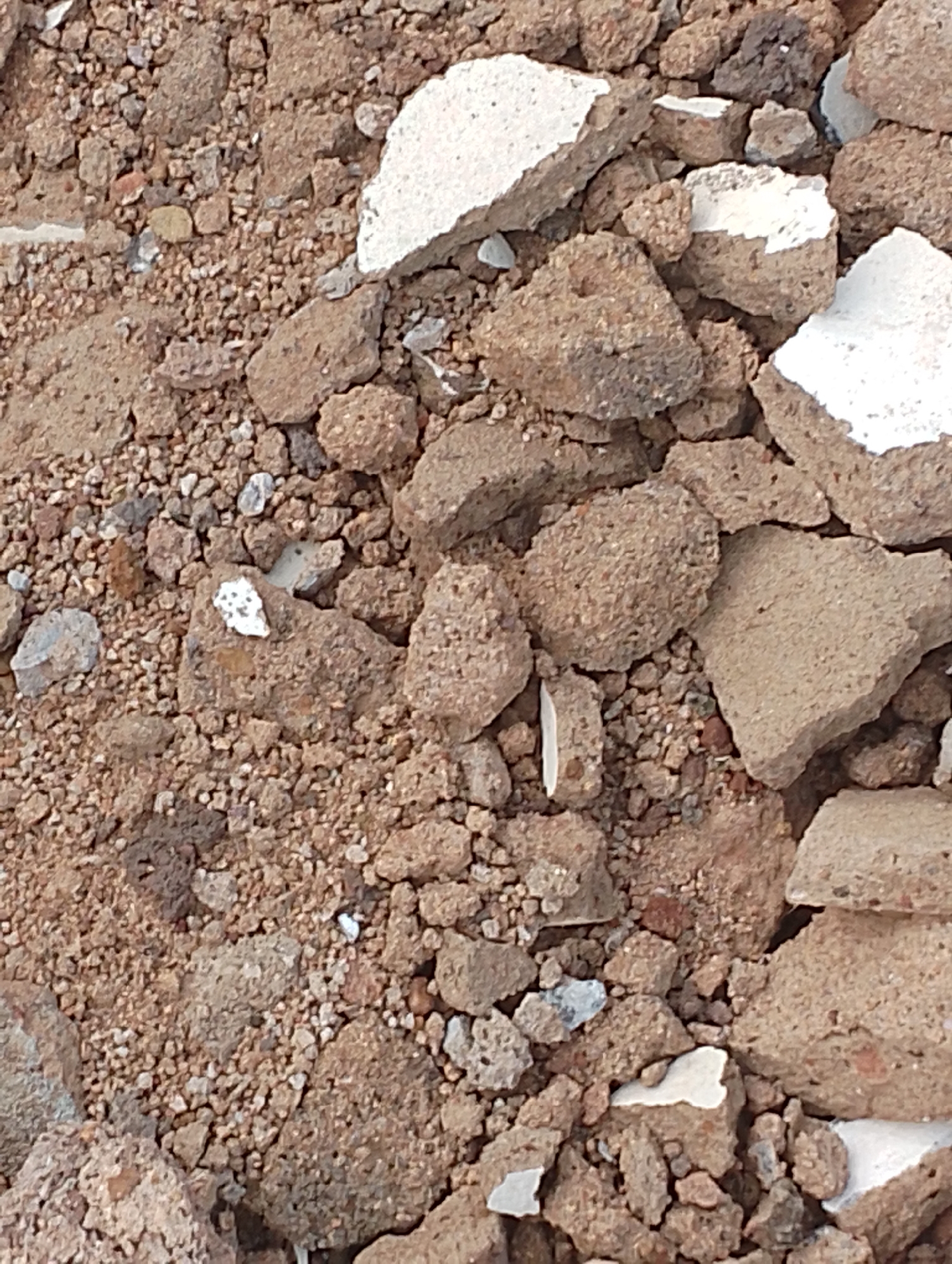 The image shows a close-up, overhead view of a pile of debris, likely from a construction or demolition site. The debris consists of broken concrete chunks, gravel, and smaller pieces of rubble. The colors are predominantly earthy browns, grays, and whites from the concrete fragments. There are no people or living subjects visible in the image. The scene is static and appears to be outdoors. The location in Jos, Nigeria is not discernible from the visual information presented in the image.