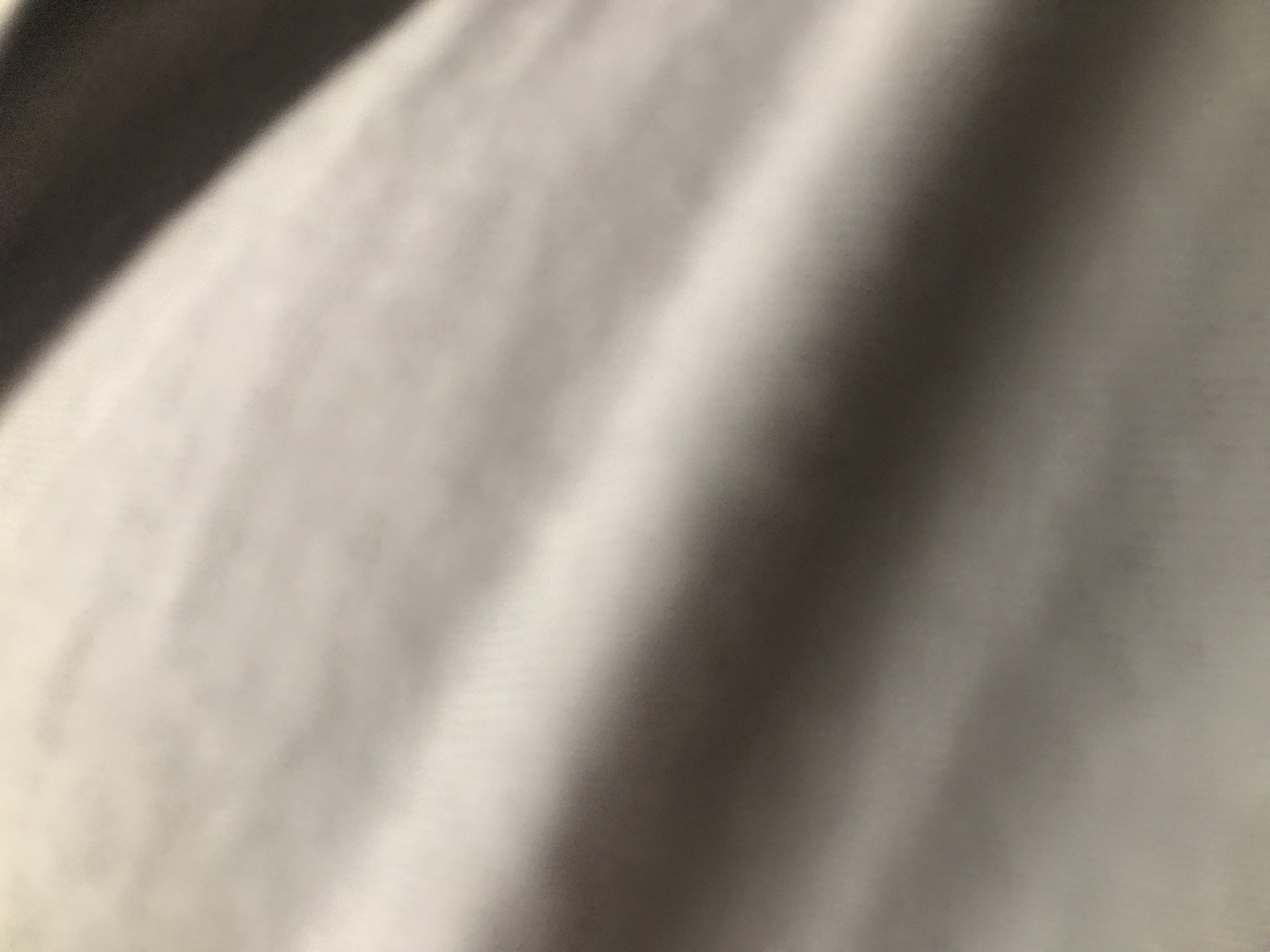 The image shows a blurred, close-up view of a fabric surface with subtle variations in light and shadow. The color is a muted gray or off-white. No specific location in Yerevan, Armenia, can be determined from the image, as it lacks identifying landmarks or features. There are no people, subjects, objects, actions, or interactions visible.