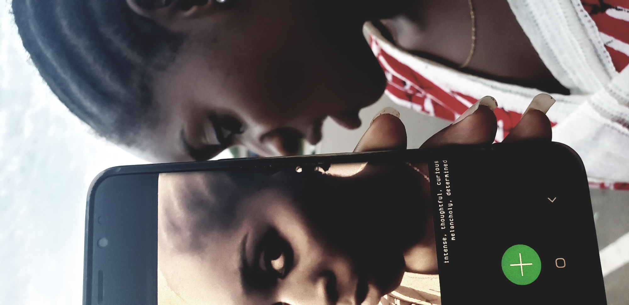 A close-up, slightly off-center photograph captures an individual holding a black smartphone vertically in an outdoor setting in Narayi, Nigeria. The right profile of the individual holding the phone is visible on the right side of the frame, showing dark skin, braided hair, a slightly open mouth, and a portion of a red and white patterned garment with a thin gold necklace. The fingers holding the phone display long, light-colored nails. The smartphone's illuminated screen displays an image of a dark-skinned woman with a shaved head or very short hair, looking intently towards the left of the screen. Overlaid on the lower portion of this image are two lines of white text: "intense, thoughtful, curious" and "melancholy, determined". Below the image and text, a green circular icon with a white plus sign, a white circular home button icon, and a white left-arrow back button icon are visible on the black interface. The background behind the subject is an out-of-focus bright sky with faint cloud formations, indicating a daytime scene.