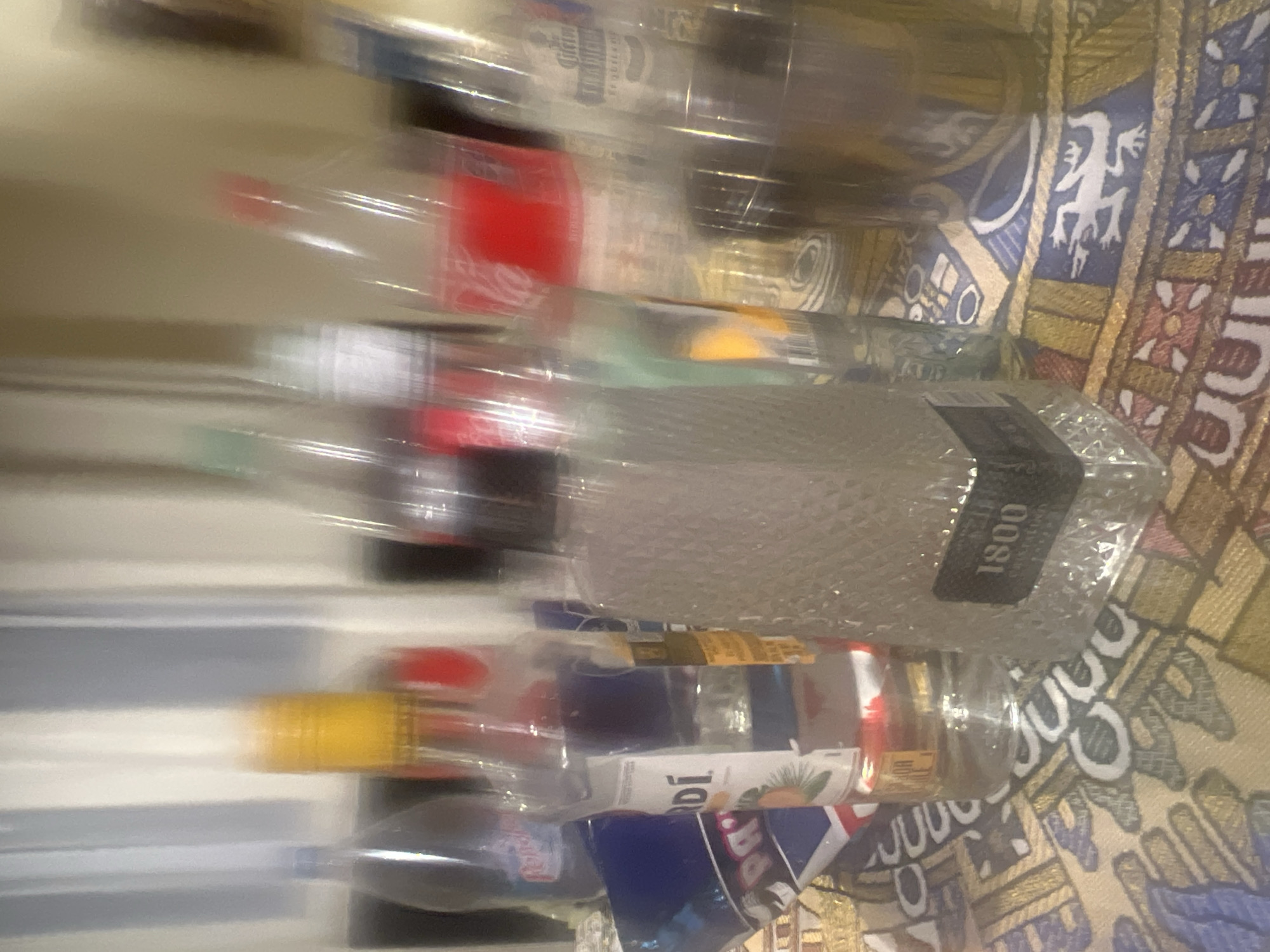 The image shows an assortment of alcoholic beverage bottles, including brands like 1800 tequila and Bacardi rum, resting on a patterned textile or surface. The setting is unidentified, and there is no information to locate it in the city of Puebla, Mexico. There are no people visible.