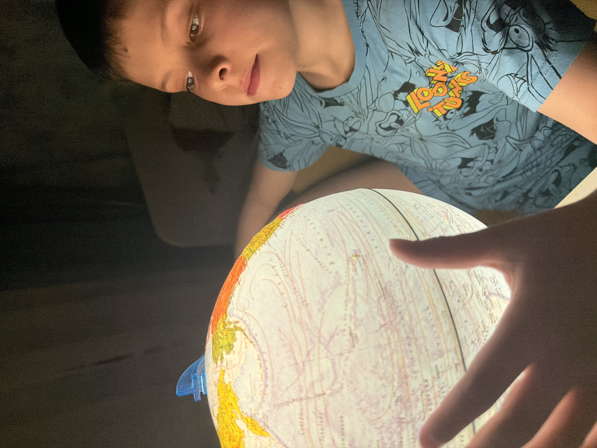 A person wearing a blue shirt is looking at a light-up globe. The person's hand is near the globe. The location is not identifiable from the image.