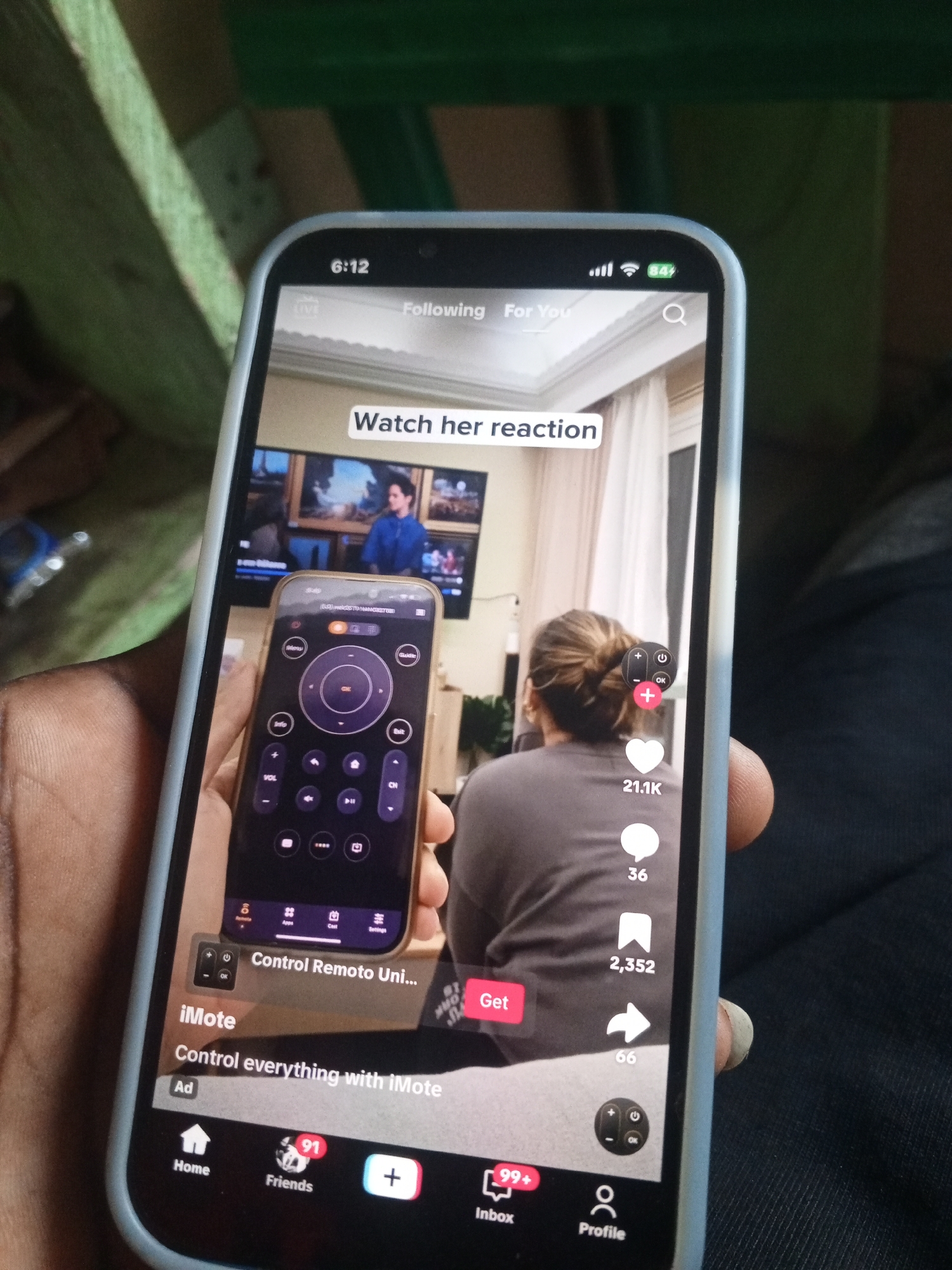 A person is holding a smartphone displaying a TikTok video. The video shows a person watching TV, while the smartphone in the foreground displays an advertisement for a universal remote app. The location in the city of Unknown, Unknown, cannot be determined from the image.