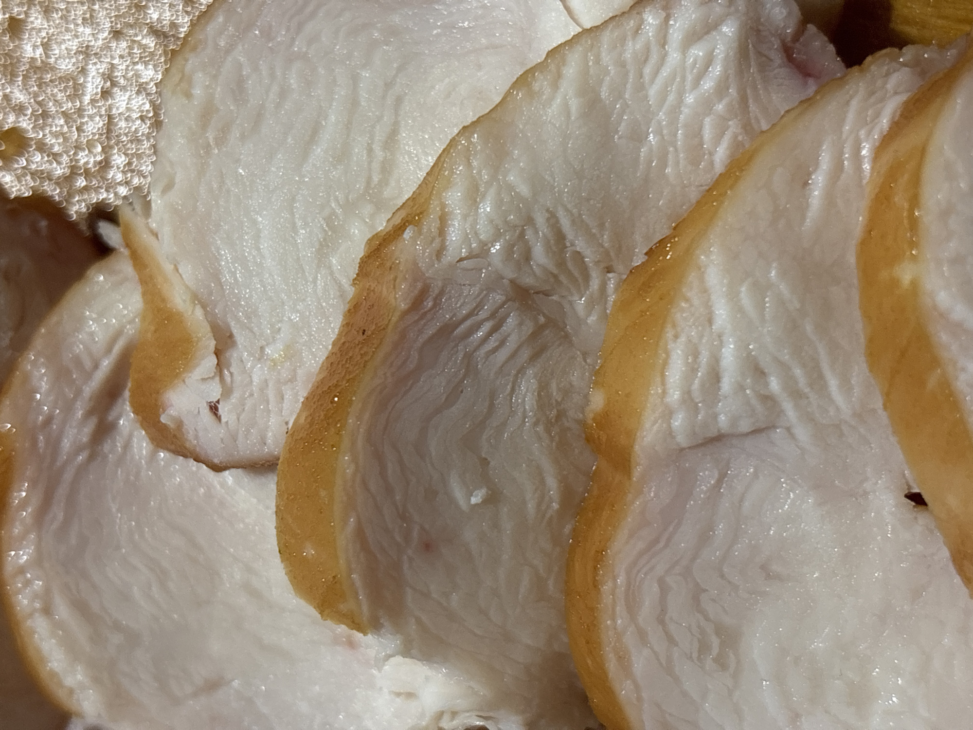 The image shows a close-up, overhead view of sliced cooked chicken breast. The chicken is thinly sliced, revealing a pale white interior with visible muscle fibers and a slightly browned, caramelized edge. The texture appears moist and tender. The arrangement suggests the chicken is prepared for serving, possibly as part of a meal or a charcuterie board. There are no people, specific locations, or environmental details visible in the image that would allow for identification of its location in Kremenchuk, Ukraine, or any other city.