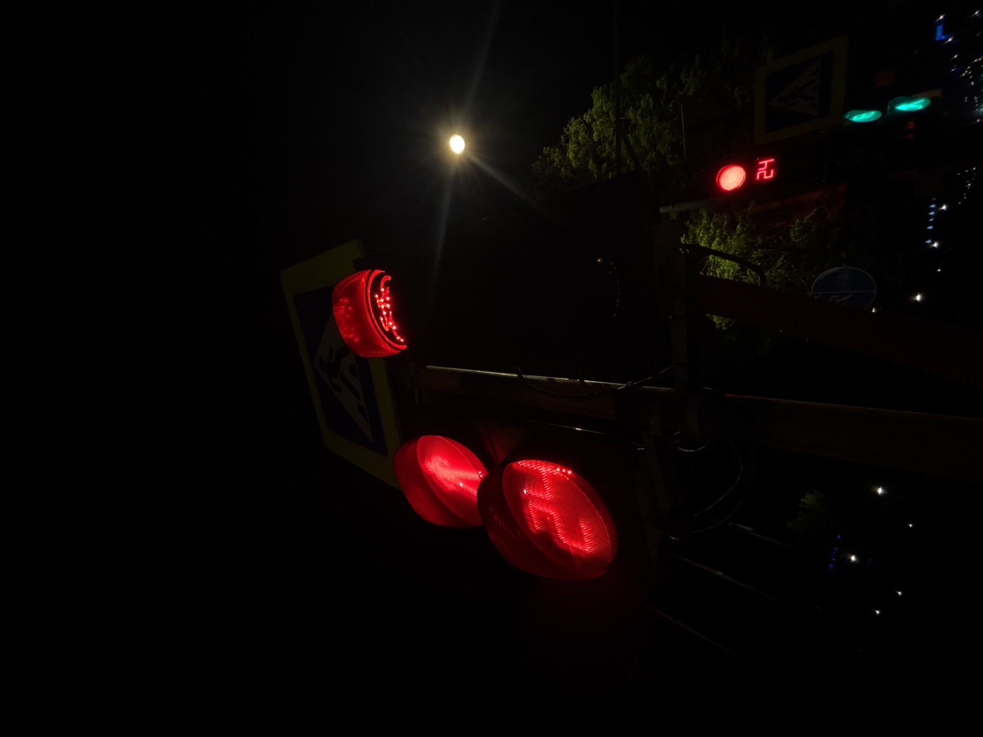 At night in Perm, Russia, traffic signals display a red light indicating "stop". The scene includes pedestrian crossing signs and the moon illuminating the sky. In addition, there appears to be a timer indicating the amount of time left until the light changes.