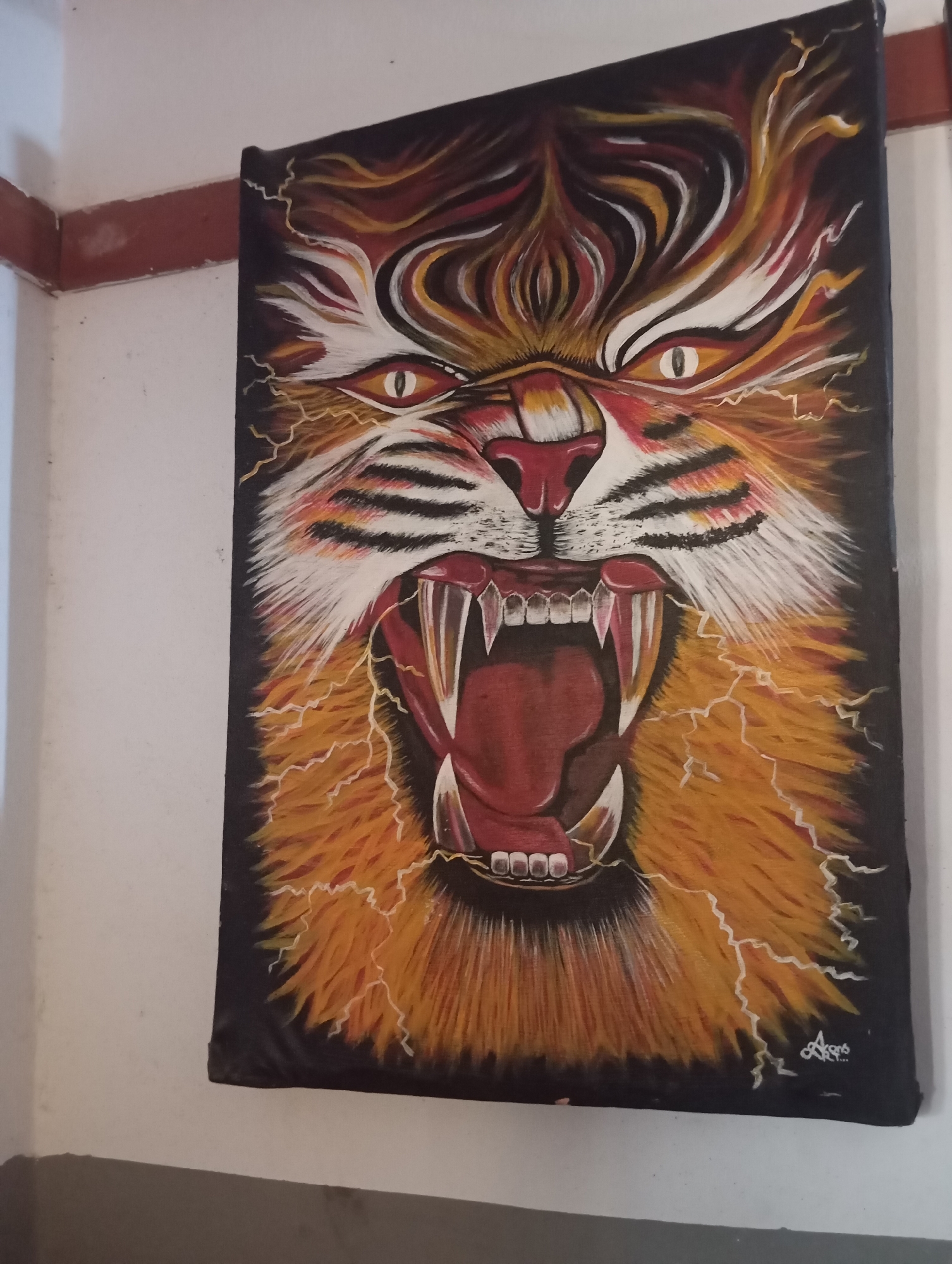 This media file contains a painting of a fierce tiger's face. The tiger is depicted with its mouth wide open, revealing sharp teeth and a dark red tongue, conveying aggression and power. Its eyes are narrowed and yellow with black pupils, adding to its intense expression. The fur around its face is rendered in shades of orange, yellow, and white, with black stripes on its nose and cheeks. Jagged lines of yellow and white, resembling lightning, radiate outwards from the tiger's face, suggesting a volatile or energetic aura. The background is predominantly black, making the vibrant colors of the tiger stand out. The painting is hung on a wall that appears to be in an indoor setting, possibly a room in a home or a gallery, with a white wall and a red trim along the top edge visible. A faint signature with the name "AKONG" and a date below it is visible in the bottom right corner of the painting. The overall impression is one of raw power and intensity. The context provided indicates this media file is located in Jos, Nigeria.