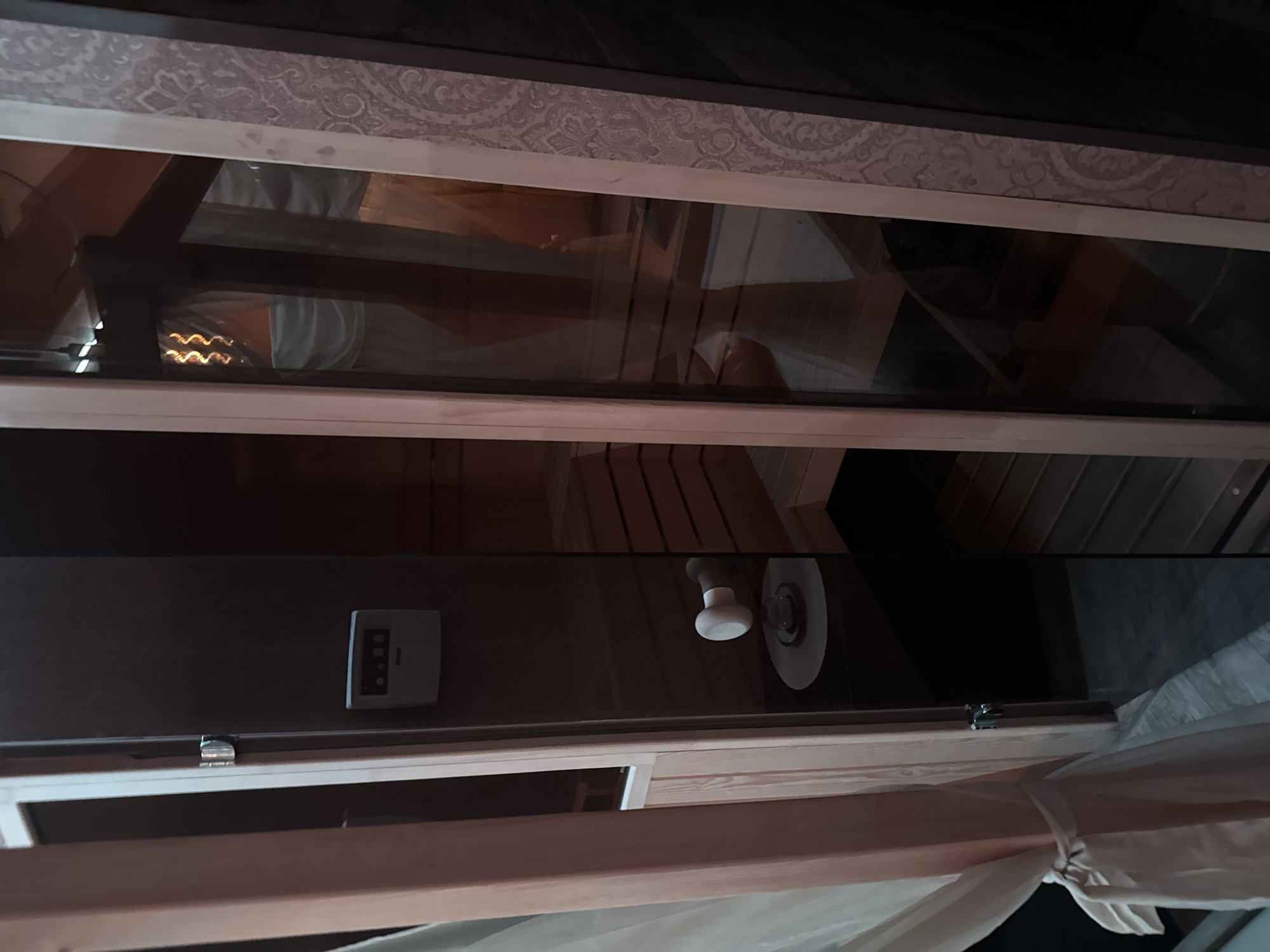 This image shows the interior of a sauna. There is a digital control panel mounted on a dark-colored wall, next to a light fixture. The sauna benches are visible through a glass panel, constructed from light-colored wood. The location cannot be identified in Sofia, Bulgaria based on provided details.