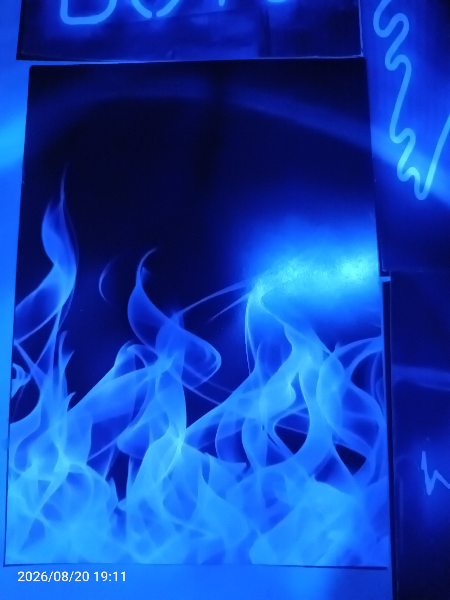 The image displays a close-up of blue flame-like patterns against a dark background. The flames are rendered in various shades of blue, with lighter, brighter areas suggesting intense heat or light sources. To the upper left and right of the central image, glimpses of blue neon lights are visible. The bottom of the image shows a date stamp: "2026/08/20 19:11". No people or specific environmental details beyond the abstract depiction of flames and neon lights are present. The location in Jawilan, Indonesia, is not visually represented in the image itself.