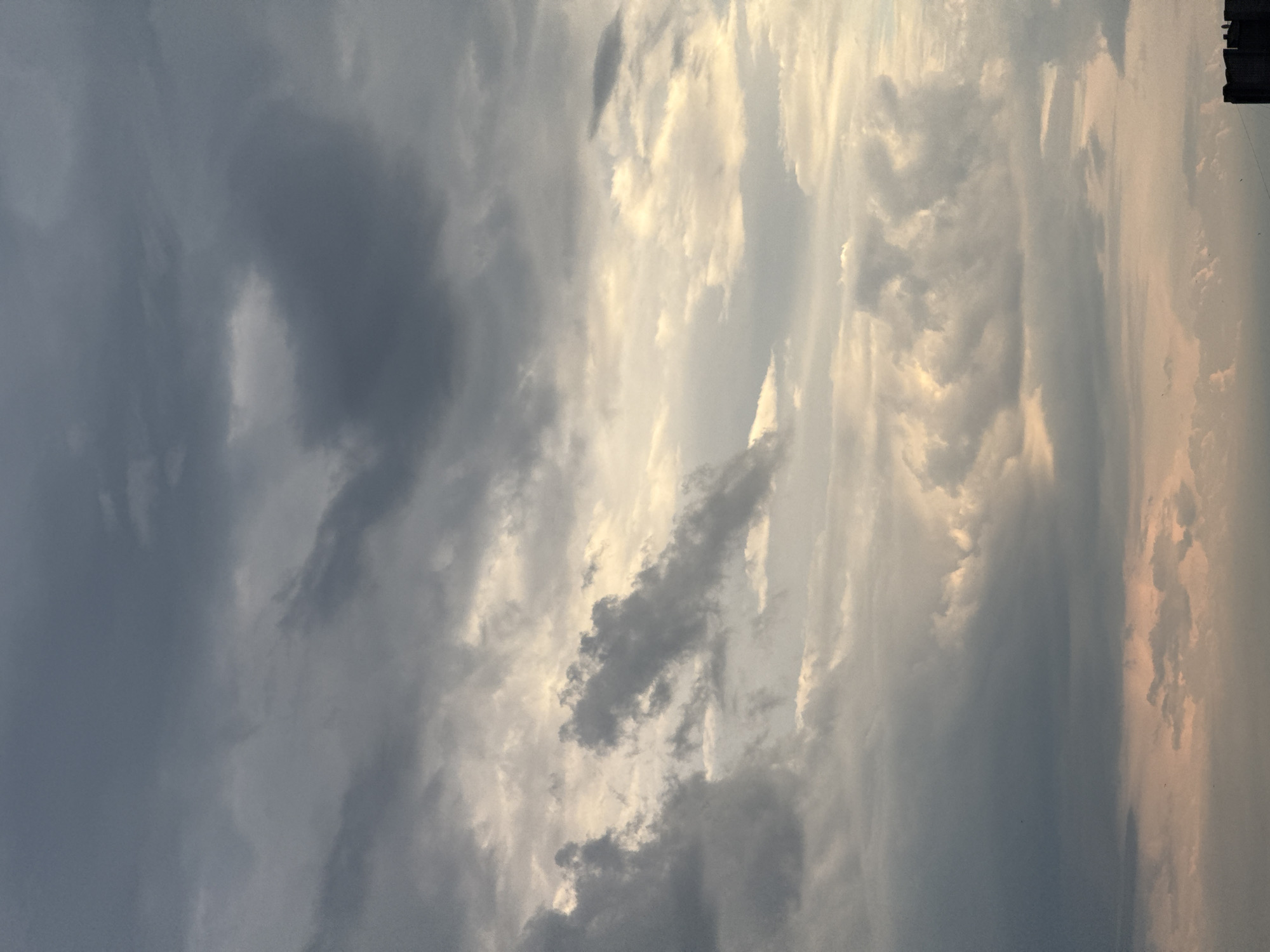 This is a photograph of a cloudy sky with a hint of sunset colors in the lower portion of the image. The clouds are dark and heavy in some areas, with lighter, more diffuse clouds above. The overall mood of the image is dramatic and slightly ominous, suggesting an approaching storm or the end of a day. There are no discernible objects or people within the frame, focusing solely on the atmospheric conditions of the sky. The location is not specified.