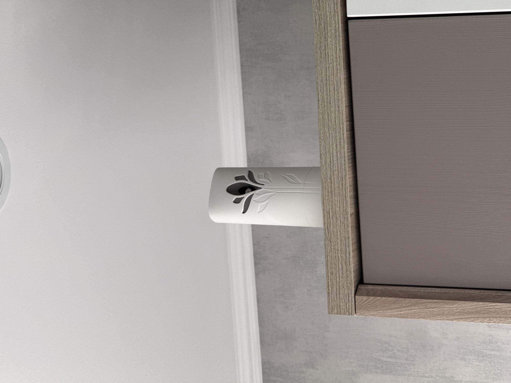 The image shows a close-up of an interior setting, likely a bathroom or kitchen, based on the fixtures and materials present. A white air freshener with a floral design sits horizontally, near a gray wall and a wooden cabinet. The cabinet appears to have a two-toned finish, with a lighter wood-grain frame and a darker gray door with a horizontal wood-grain pattern. The location is undetermined but the claim of Lovech, Bulgaria is unconfirmed based on the given visual information.