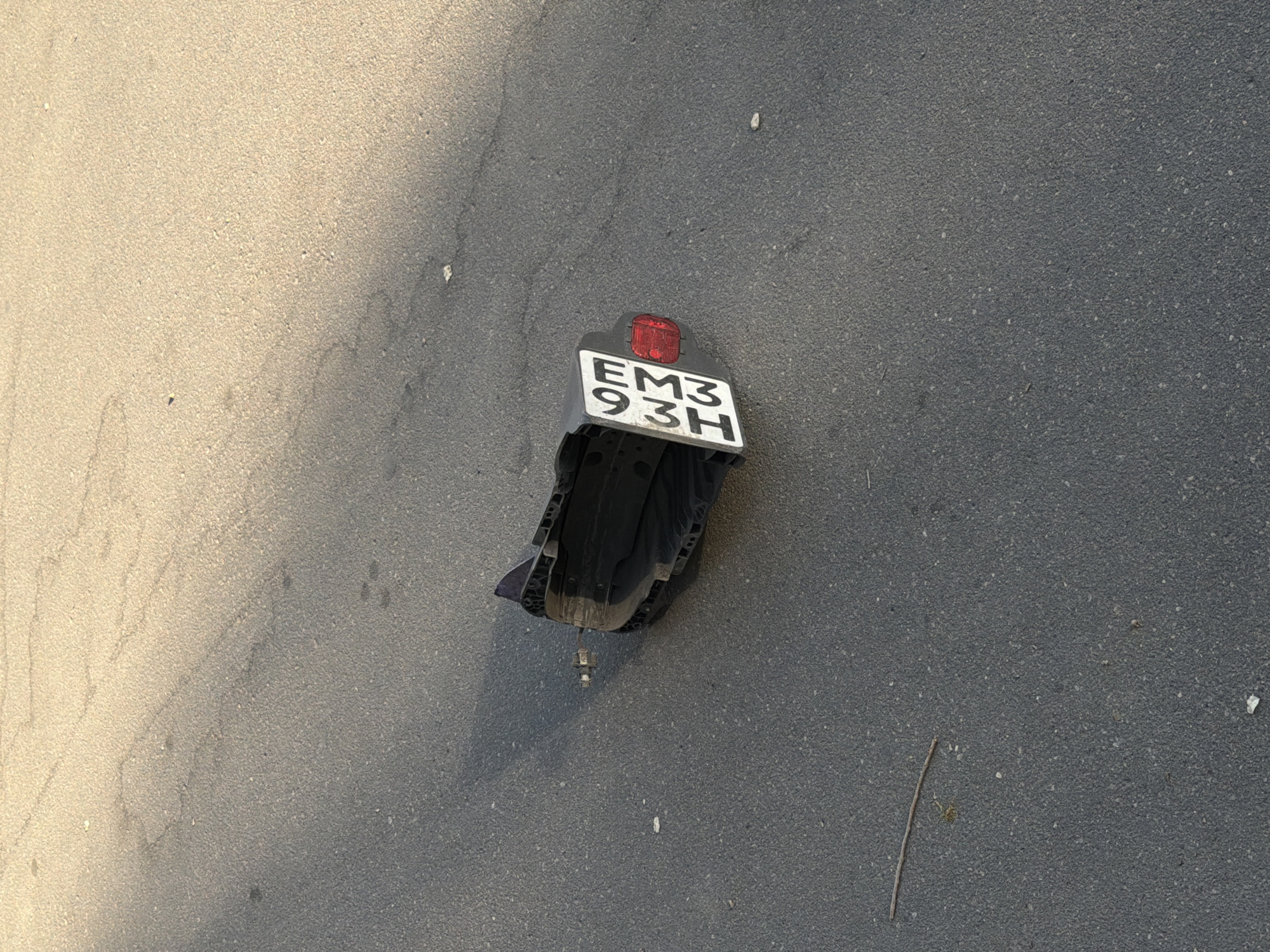 The image shows a broken motorcycle fender with a license plate reading "EM3 93H" lying on asphalt. The scene appears to be outdoors on a paved surface. While the license plate may provide clues, the image doesn't contain enough information to confirm the location is Khimki, Russia.