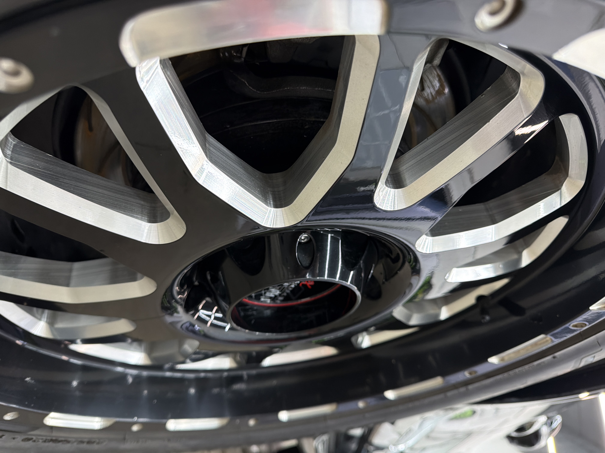 The image shows a close-up of a black and silver aftermarket car wheel. The wheel has a multi-spoke design, with alternating black and silver spokes. The center cap is black and features a small design in red. The brake disc is visible behind the wheel. There is no evidence in the image to suggest it was taken in Krasnoyarsk, Russia.