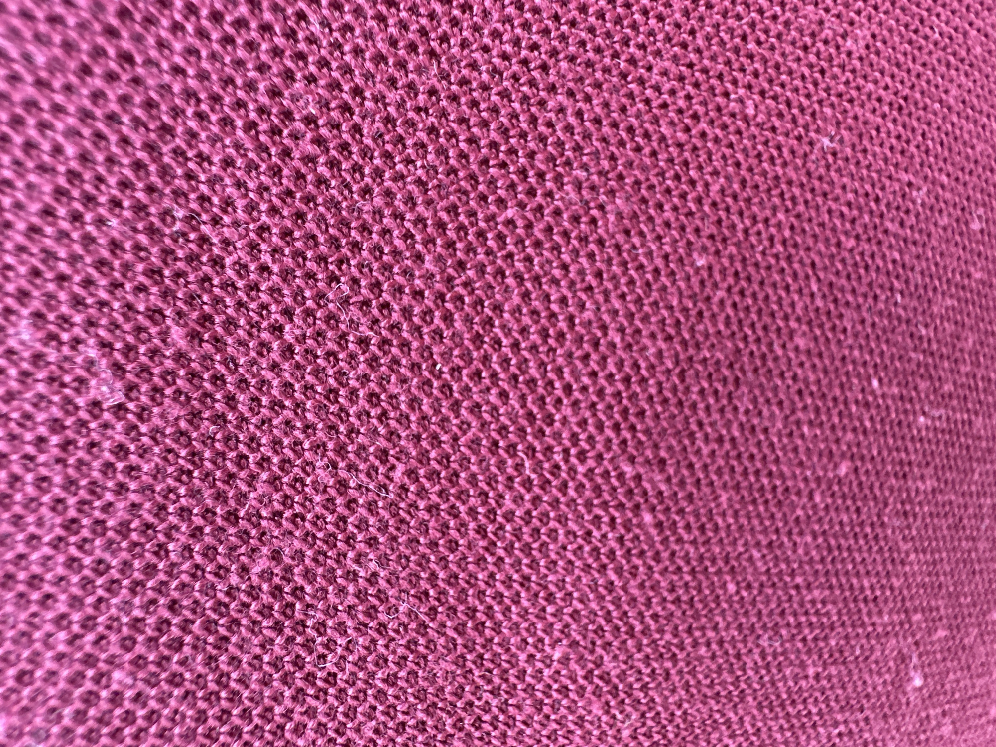 The image depicts a close-up view of a burgundy-colored knitted fabric. The weave is tight and uniform, creating a textured surface. There are small fibers protruding from the knitted structure, giving the fabric a slightly fuzzy appearance. The image lacks discernible features that would link it to Bac Nha Trang Ward, Vietnam. There are no people, subjects, objects, actions, or interactions evident other than the fabric itself. The environment is limited to the fabric's surface and lacks any contextual elements.