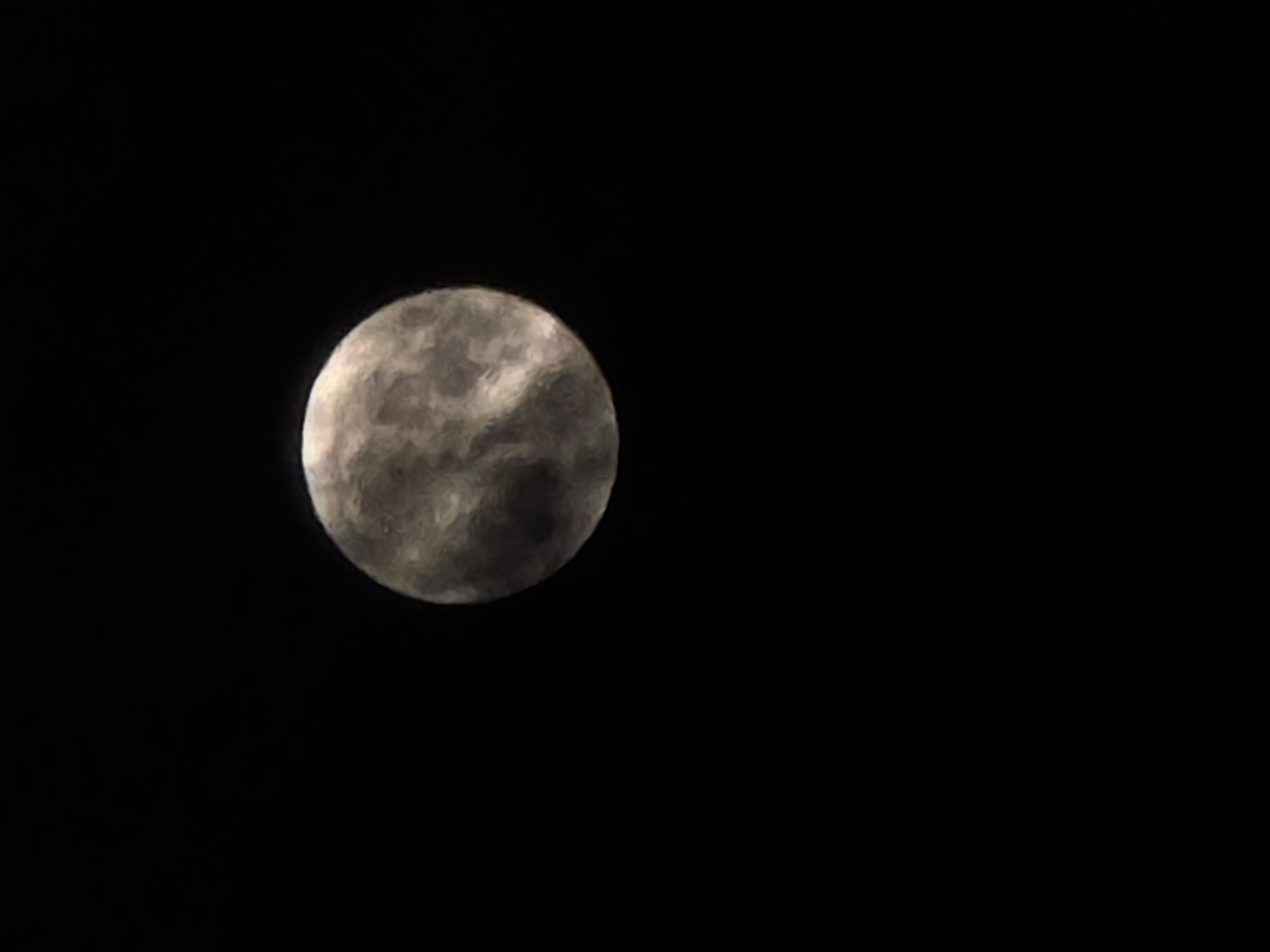 The image shows a full moon in a dark sky. The moon is off-center to the left. There are no other objects or subjects visible in the frame. The environment is dark and appears to be at night.