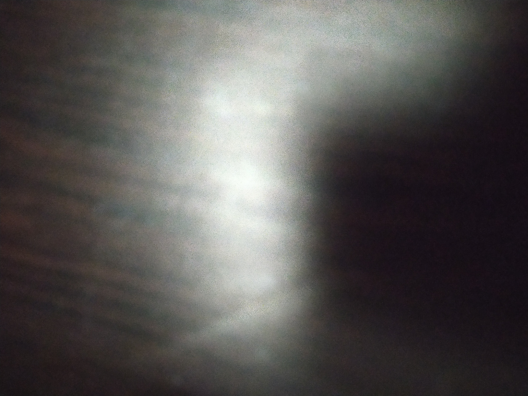 The image depicts a blurred, low-resolution scene dominated by light and dark areas. A vertical swath of diffused light occupies the center, fading into darker regions on either side. The texture suggests a grainy or possibly fog-filled environment. The image is too indistinct to identify people, subjects, objects, actions, interactions, or any specifics about the location in the city of Unknown, Unknown.