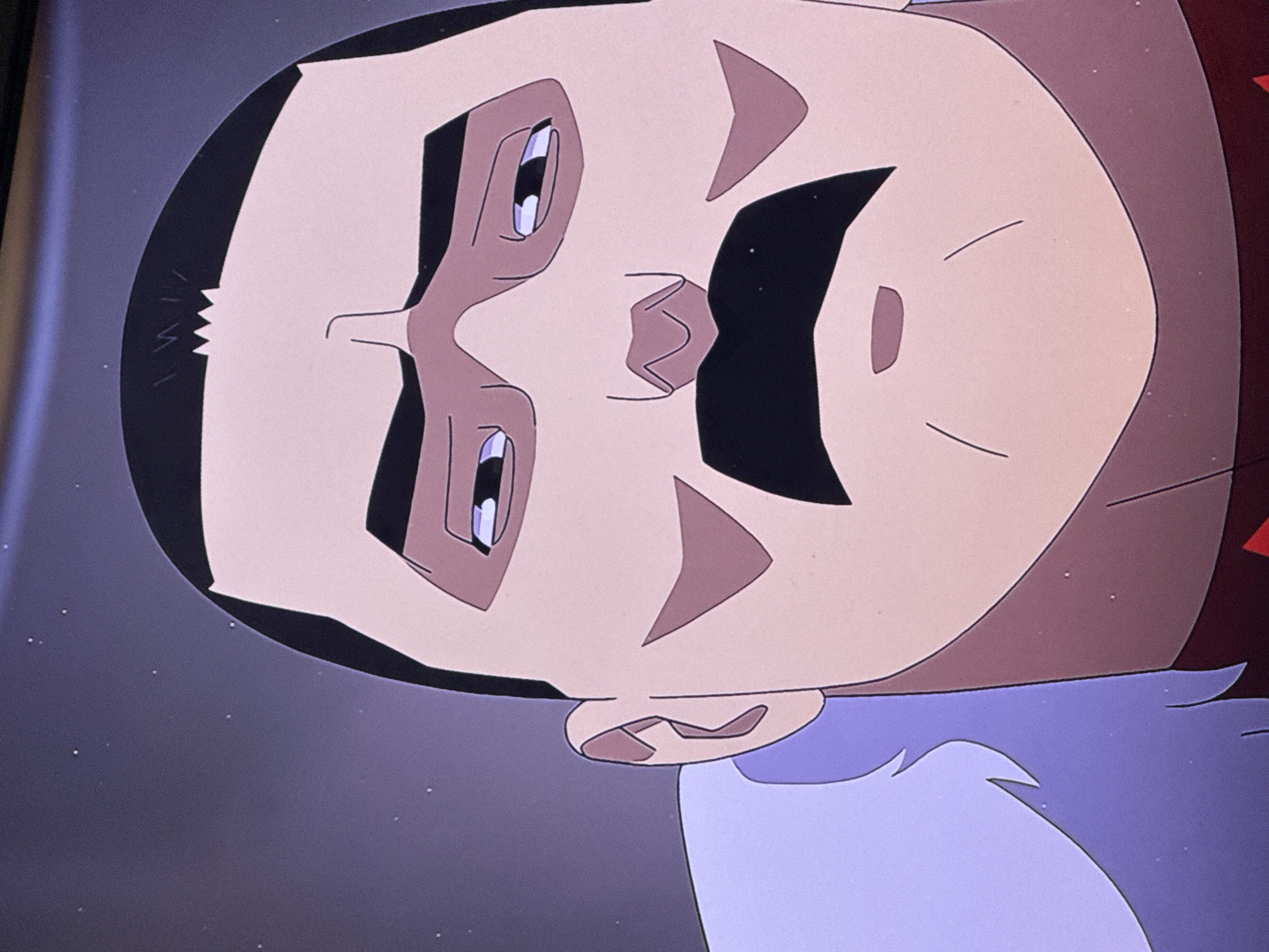 The image shows a close-up of a cartoon character's face, rendered in a flat, graphic style. The character has a dark, rectangular mustache, a dark, rectangular haircut with a jagged hairline, and pale skin. Their eyes are elongated with visible irises. The character wears a high collar or garment of a muted brown and purple color. The background is dark with scattered white dots. There is no visible indication of the city of San Bernardino Tlaxcalancingo, Mexico.