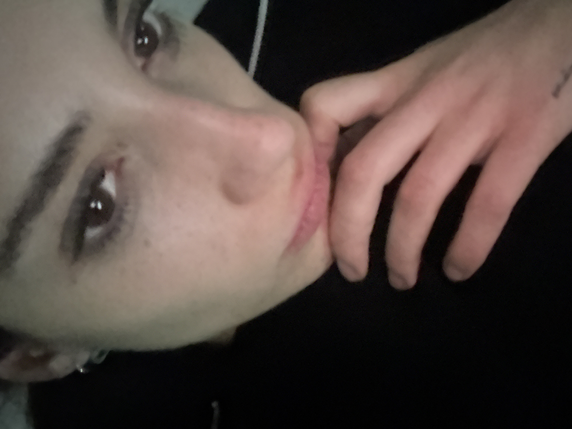 A close-up, slightly angled shot of a person's face and hand. The person has fair skin, brown eyes, and dark eyebrows. Their fingers are touching the right side of their mouth. There is a tattoo on their right hand. The person is wearing a black shirt. The background is dark.
I cannot determine the location in Buenos Aires, Argentina from this image.