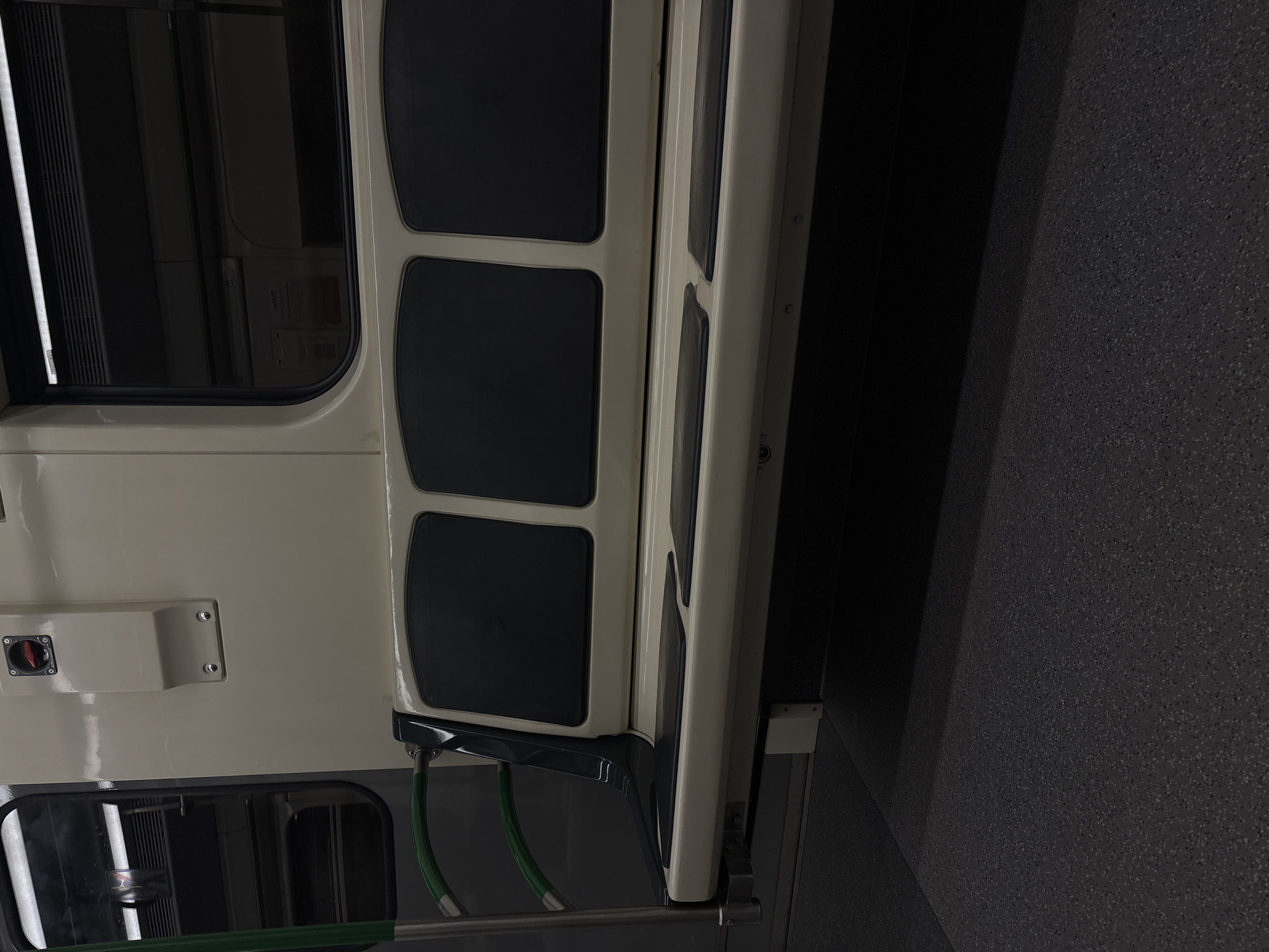 The image depicts the interior of a subway train in Sofia, Bulgaria. Visible elements include the train's door with three dark windows, a beige interior panel, green grab handles, and a gray floor. The scene appears unoccupied.