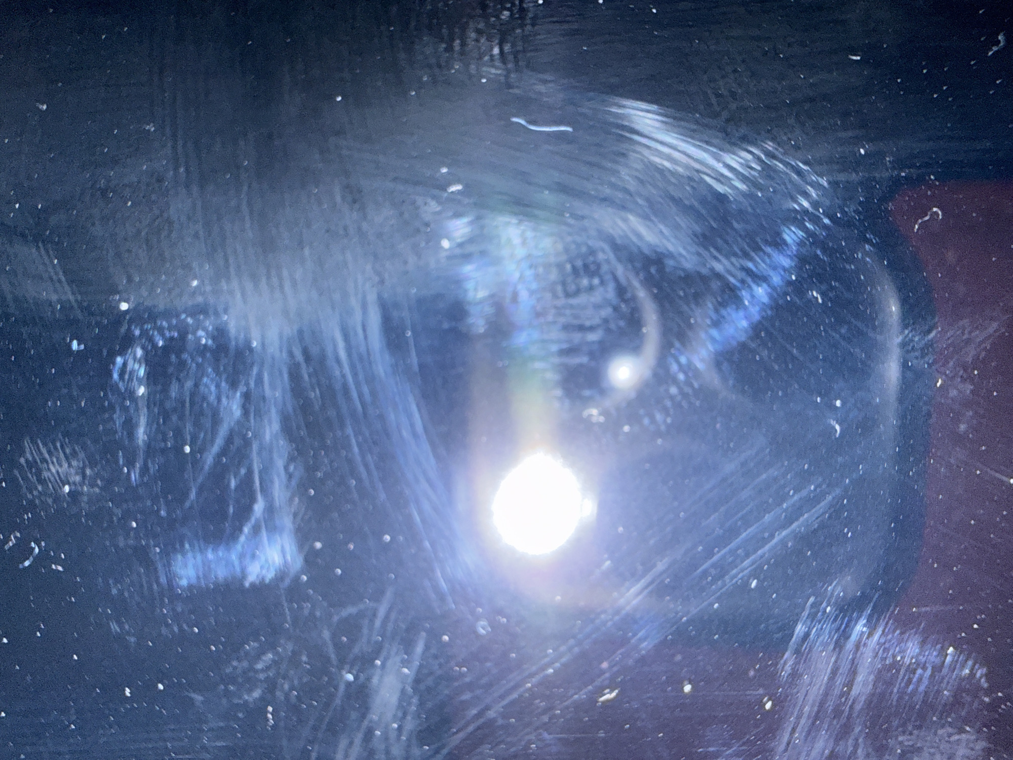 The image shows a dark, possibly reflective surface marred by numerous scratches and streaks. A bright, circular light source is located in the center of the frame, creating intense glare and obscuring details behind it. The overall texture is gritty and unclear due to the surface imperfections. The environment and any specific location details, including the city of Lovech, Bulgaria, are not discernible from the visual information provided.