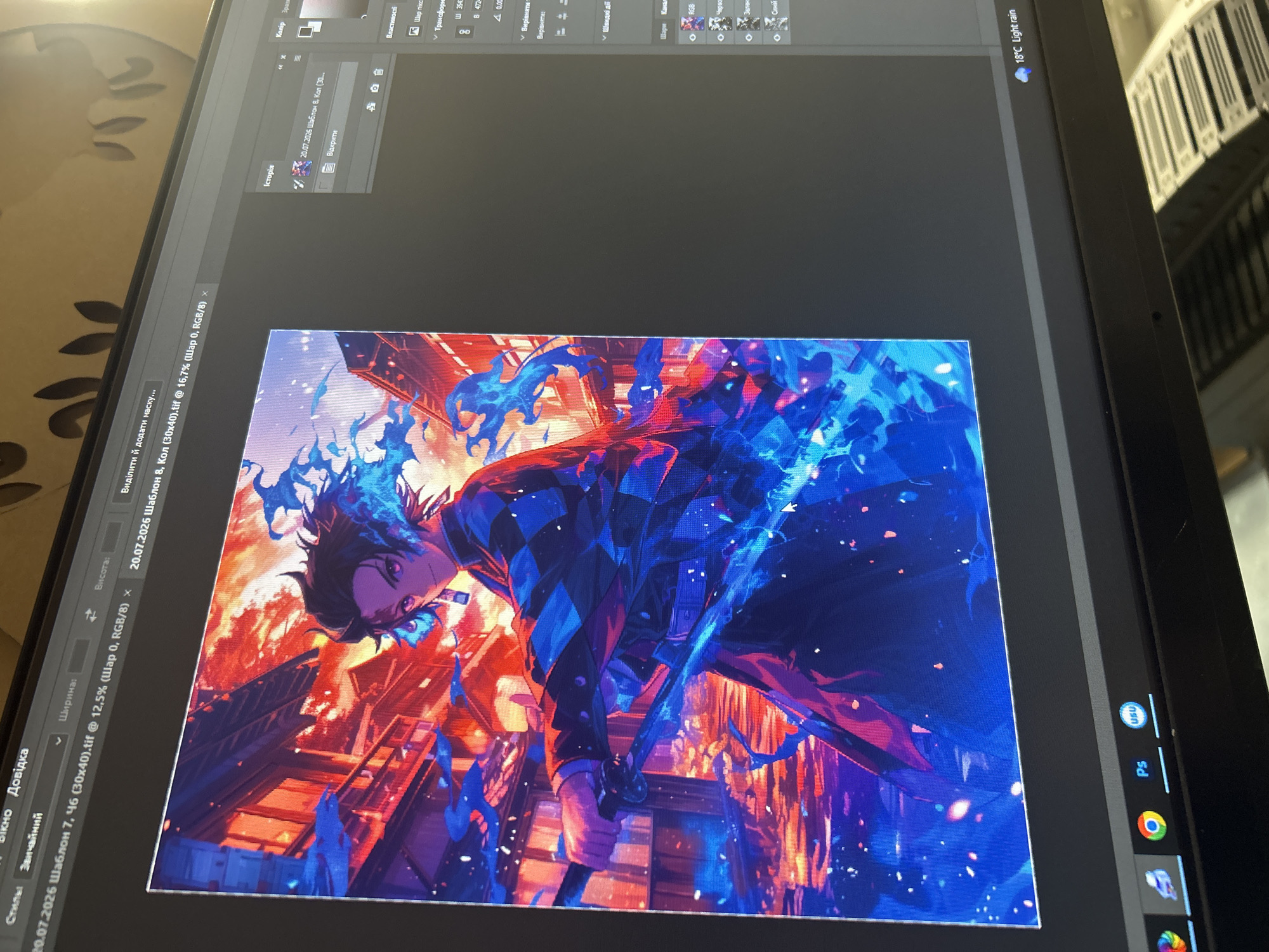 The image shows a computer monitor displaying a digital artwork of an anime character. The character, a young male with dark hair and purple eyes, is dressed in a black and checkered haori with blue flames emanating from his body and sword. He is holding a katana with a blue flame effect. The background is a vibrant scene of traditional Japanese architecture with red buildings and a fiery sky.
On the right side of the monitor, a Photoshop interface is visible, displaying panels such as "History," "Color," "Properties," and "Layers." The currently open document is named "20.07.2026 Шаблон 8, Кол (30x40).tif."
The bottom taskbar of the operating system shows icons for Google Chrome, Adobe Photoshop, and another application. In the bottom right corner of the screen, the weather information indicates "18°C Light rain."
There is no specific information in the image to identify the location within the city of Ternopil, Ukraine. The image captures a user's screen while working on a digital art project.