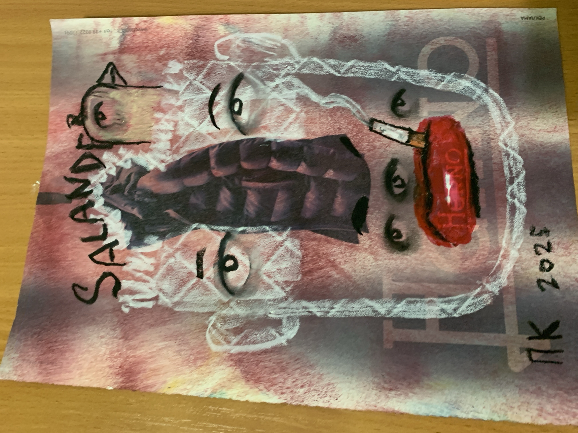 The image displays a collage or artwork featuring a stylized face. The background has a textured, reddish-pink and purple gradient. Prominently featured in the center is a dark puffer jacket, partially obscuring a nose. Above the jacket, the word "SALANDER" is written in black, stylized letters. To the right of "SALANDER" is a drawing of a bird-like head with a single eye. The face itself is outlined in white chalk or pastel, with two large eyes drawn above the jacket. Below the jacket are two smaller eyes, and a pair of bright red lips with a cigarette in them. The cigarette is lit and emitting smoke, also rendered in white. The bottom left of the artwork shows the initials "PK" and the year "2025" written in black. A faint, translucent overlay of large letters, possibly "F" and "I", can be seen behind the face. On the far right edge of the artwork, in small text, are the words "РЕКЛАМА" (which means "advertisement" in Russian) and a phone number. The artwork is placed on a wooden surface, likely a table. The image does not contain any elements that indicate a specific location in the city of Kirov, Russia.