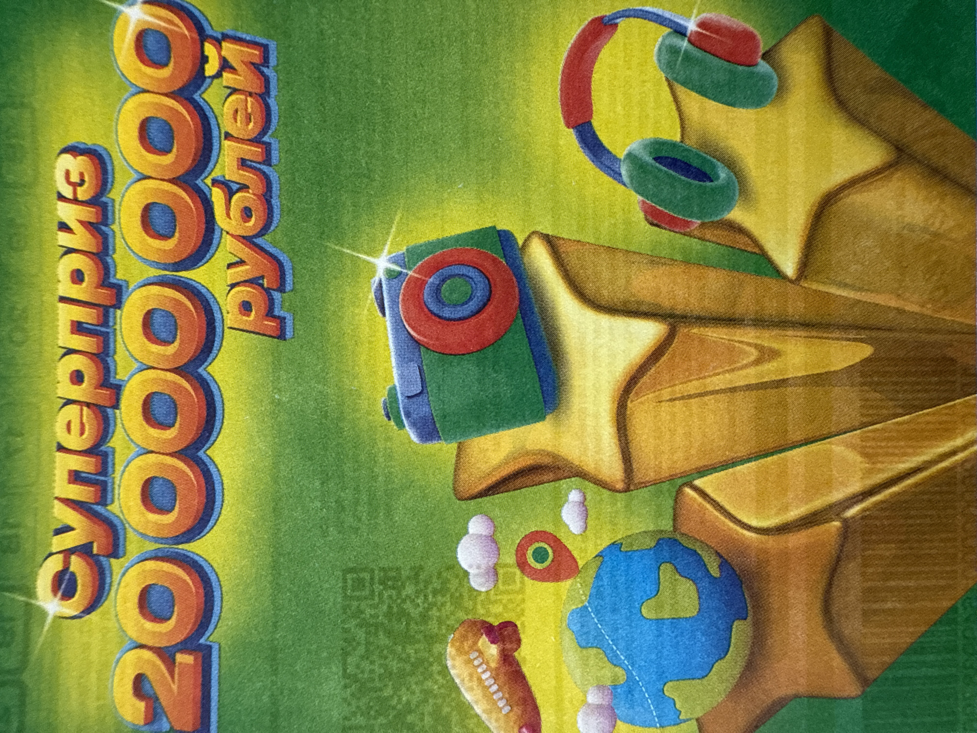 The image is a promotional graphic featuring cartoonish depictions of various objects, predominantly in shades of gold, green, blue, and red, against a green backdrop.
On the left, text is vertically oriented and appears to state "Суперприз 200000 рублей," indicating a super prize of 200,000 rubles.
The right side of the image is dominated by stylized, golden stars. Atop one star is a pair of headphones, with red earcups and green earpieces. Another star has a green object on it with a red circle and a blue circle on the inside of the red circle. At the bottom are a globe, a pair of white puffy clouds, and a light yellow rocket with pink accents.
A QR code is in the bottom left of the image.
There is no information in the image indicating the location in the city of Votkinsk, Russia. The image primarily depicts an advertisement or promotional material without any clear geographical identifiers.
