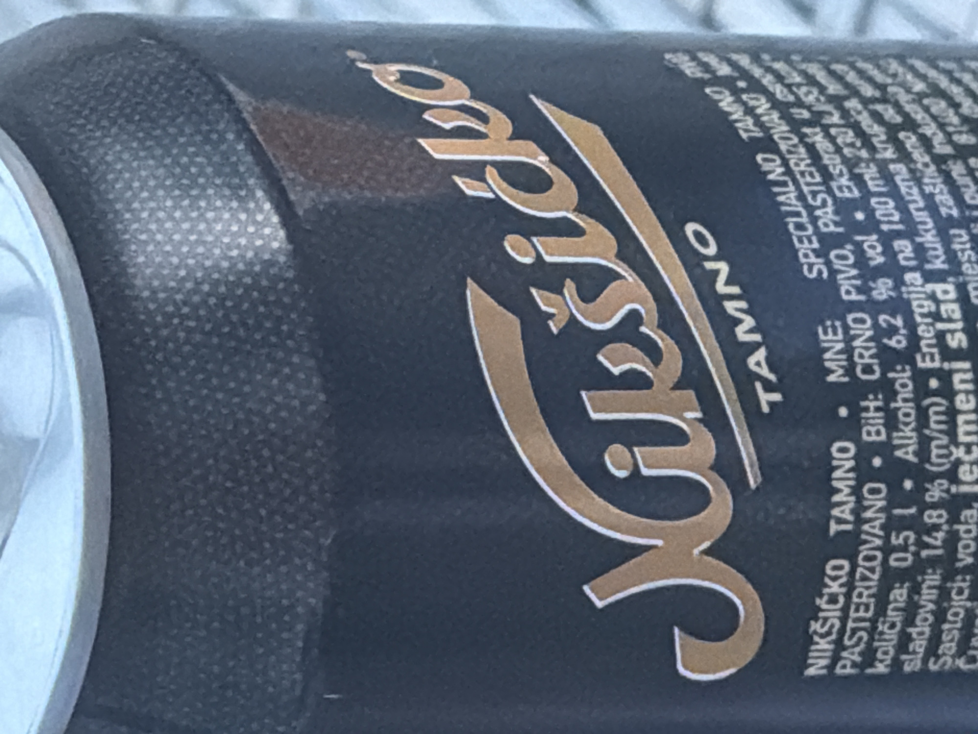 A close-up image shows a partially visible can of Nikšićko Tamno dark beer. The can is black with gold lettering. The label indicates it's a "Specialno Tamno Pivo," which means "Special Dark Beer." It's pasteurized. It contains 6.2% alcohol by volume. The label lists the ingredients as water, barley malt, and corn grits.
