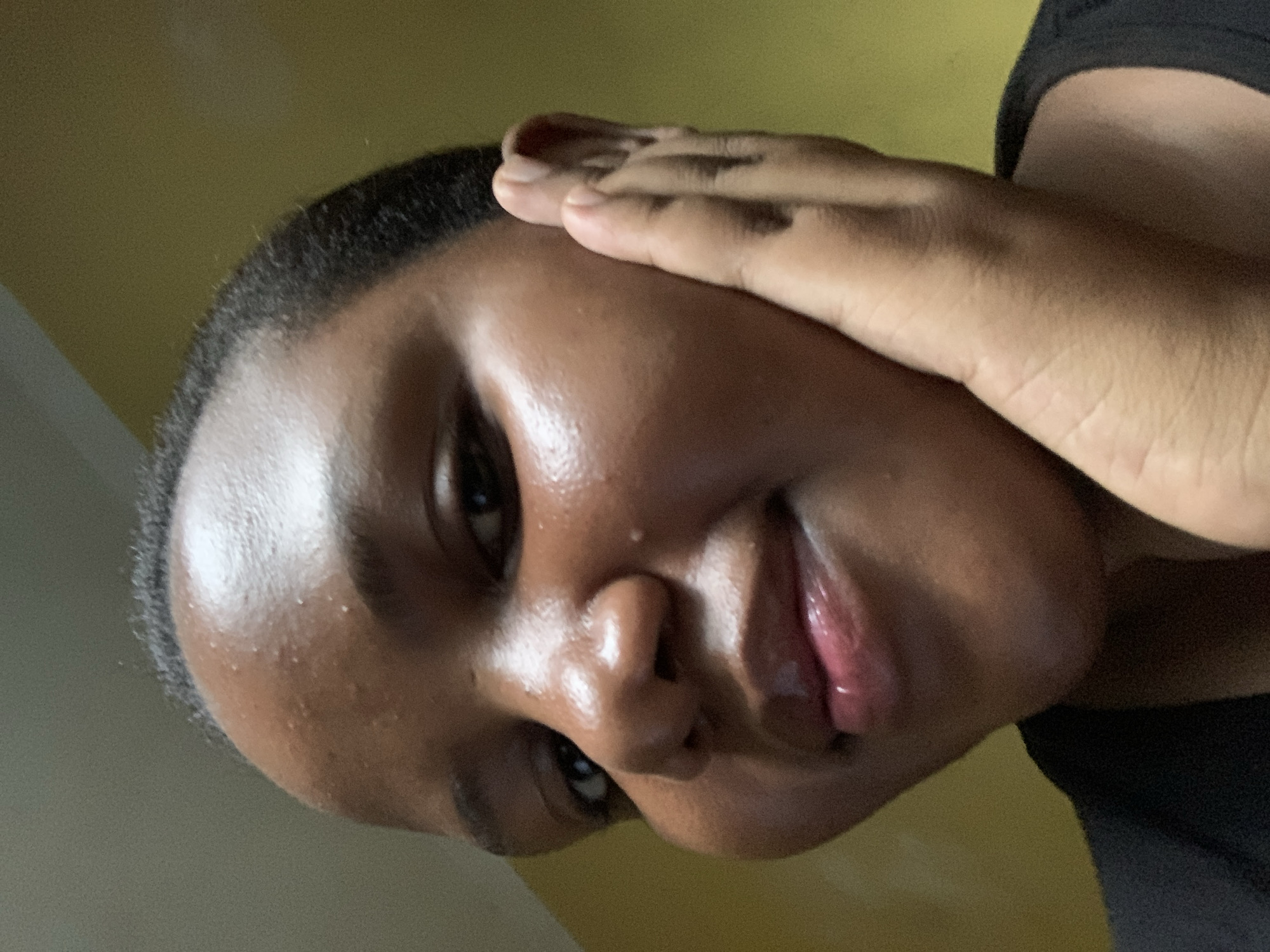 A close-up portrait of a dark-skinned person with short, dark hair is visible. They have a hand resting on their forehead and cheek. The background is a yellowish color. There are no elements indicating a specific location in Dar es-Salaam, Tanzania.