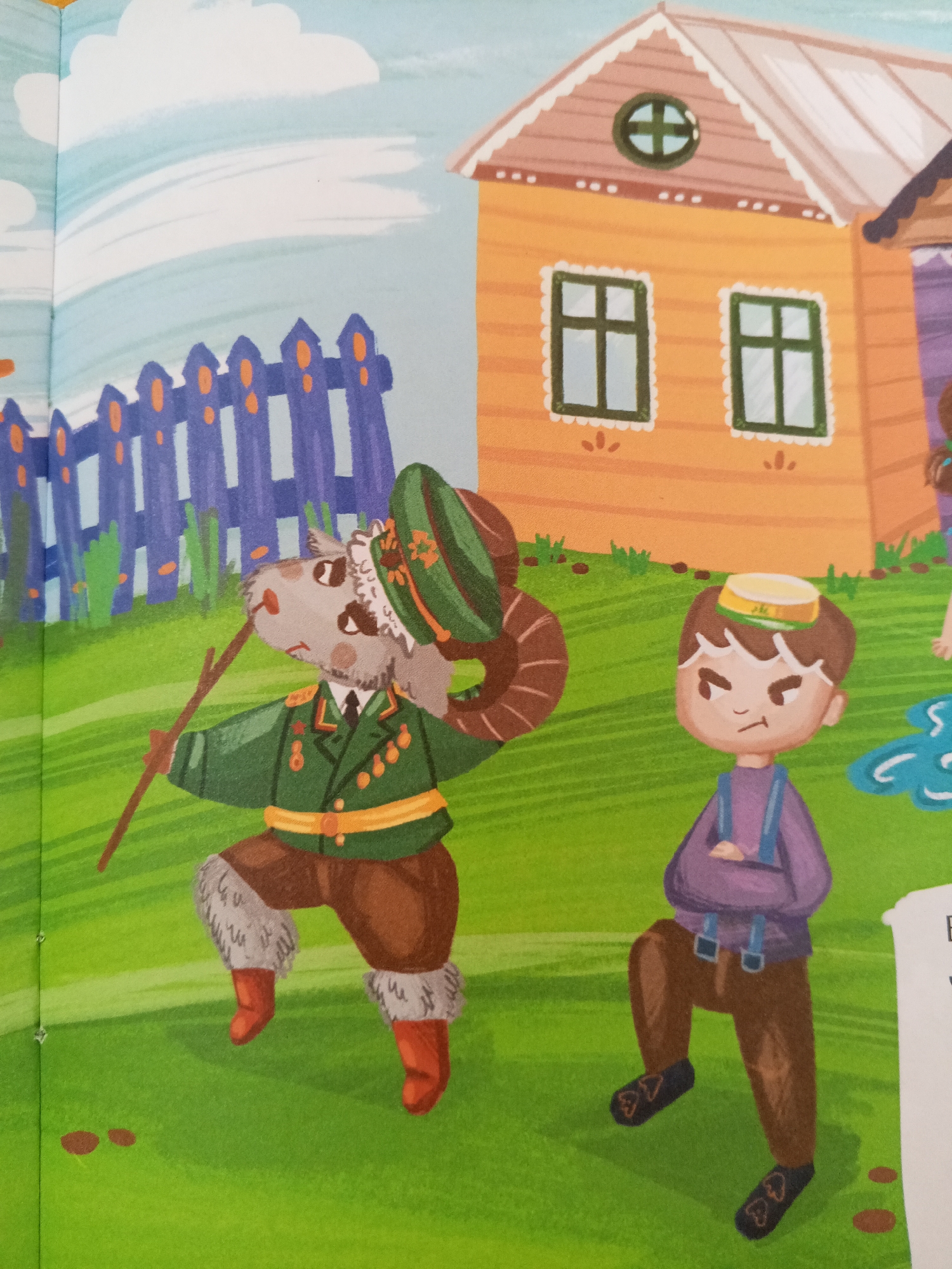 The image is an illustration from a children's book. A ram wearing a military-style uniform, including a hat, jacket with medals, and fur-lined boots, stands in a grassy field holding a stick. To the right, a young boy in overalls and a cap stands with his arms crossed, looking displeased. In the background, a fence and a stylized orange house with windows and a roof are visible. The scene is set in a park or garden, possibly in the city of Chistopol, Russia.