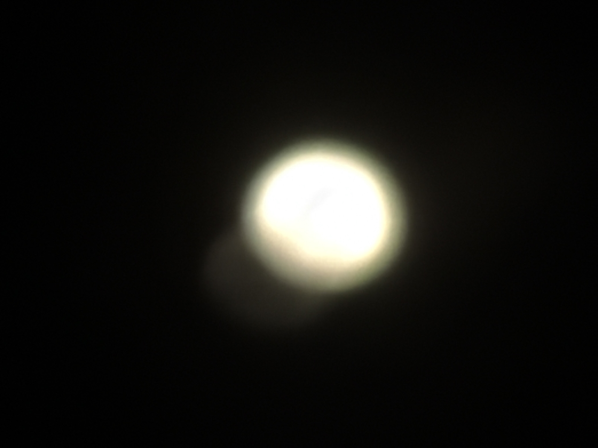A blurry, circular, bright light source is centered against a dark background. No specific location, city, people, objects or actions are discernible.