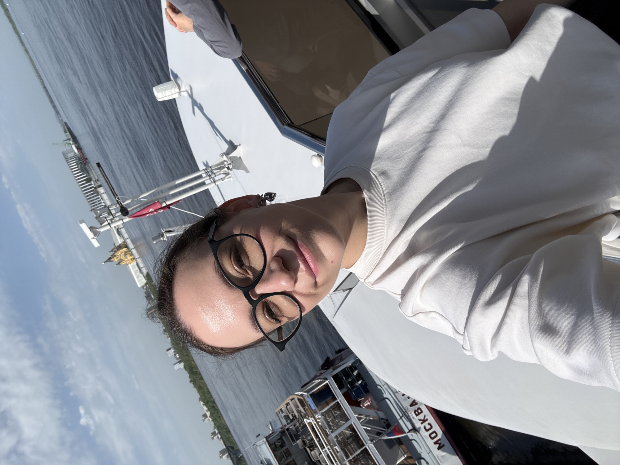 A person with glasses is on a boat on the Volga River in Nizhny Novgorod, Russia. The boat is white and has the word "Москва" (Moscow) on it. The river is visible in the background, with buildings and trees on the shore.