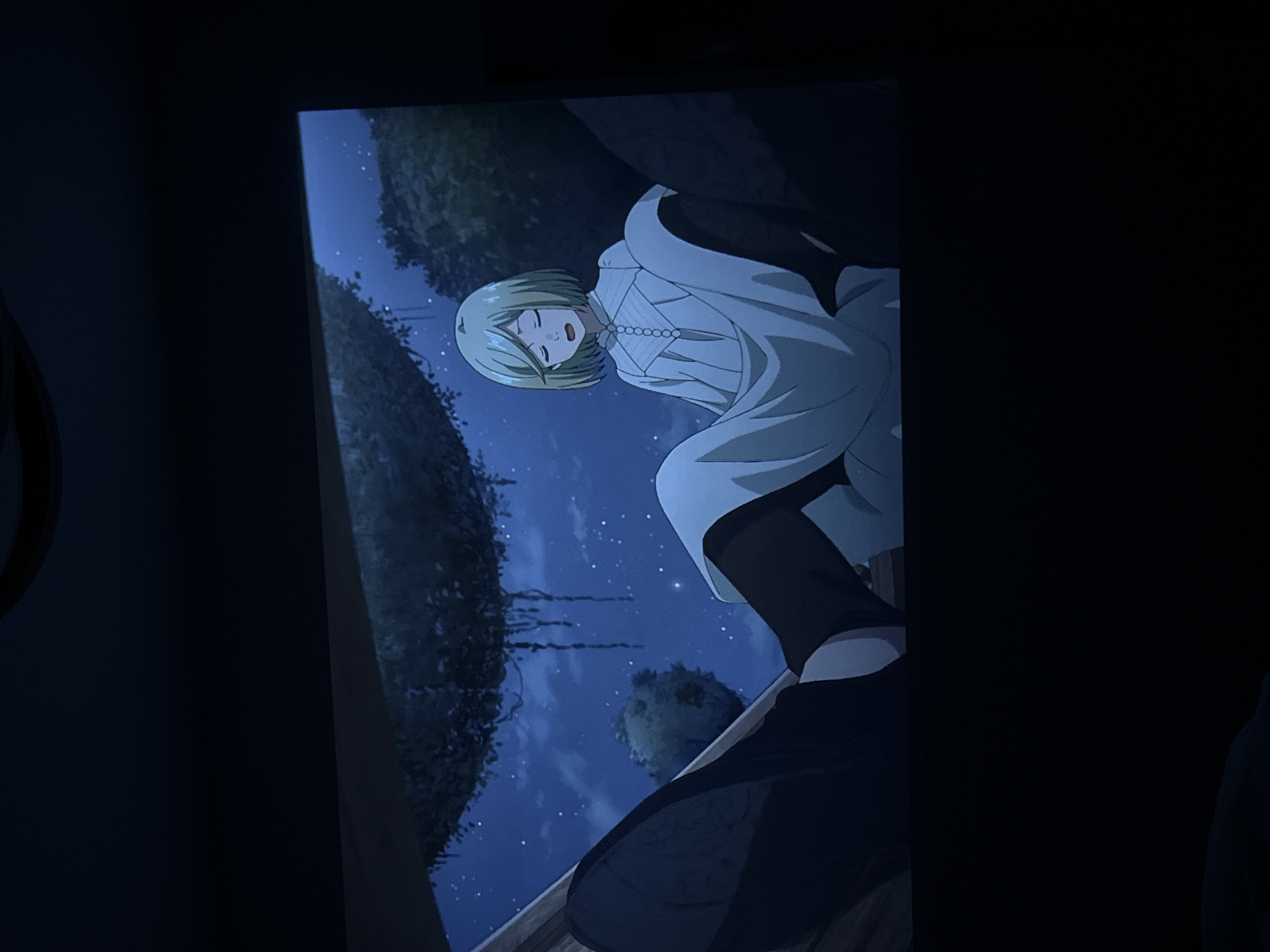The image shows an anime character with short, light blonde hair, wearing a white kimono-style robe with a pearl necklace. The character is positioned against a background featuring a night sky with visible stars, trees, and what appears to be a stylized landscape. The setting seems to be outdoors, possibly on a boat or a dock. The location is not Krasnoyarsk, Russia, as it is an anime scene.