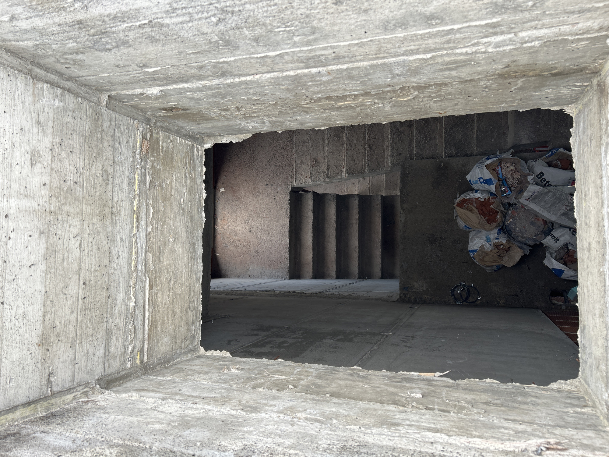 From a concrete opening, a view of the interior of a building is visible. Concrete stairs lead downward. Piles of debris bags are in the lower right corner. The location is Sofia, Bulgaria.