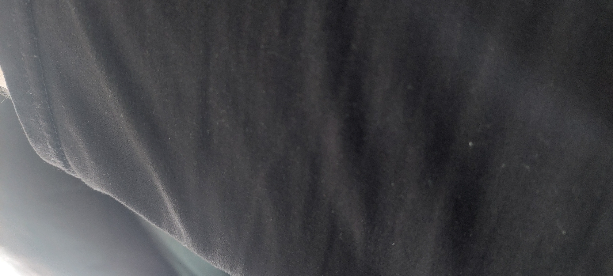 The image shows a close-up view of a wrinkled black fabric. The lighting suggests an outdoor setting, with a bright light source coming from the upper left, casting shadows and highlighting the texture of the fabric. The fabric appears to be soft and possibly worn. There are no discernible people, objects, or actions within the frame. The scene is devoid of any specific location indicators, and therefore, cannot be placed within the city of Berod bei Hachenburg, Germany.