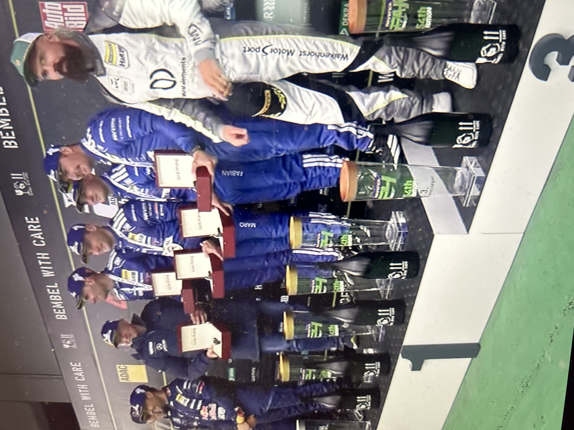 The image shows a group of people on a podium, presumably celebrating a victory. The podium is marked with "11" and "3", indicating positions. The people are wearing racing suits, suggesting they are likely race car drivers. They are holding trophies or awards. The environment appears to be a racing track. The location in Sofia, Bulgaria, is not discernible from the image.
