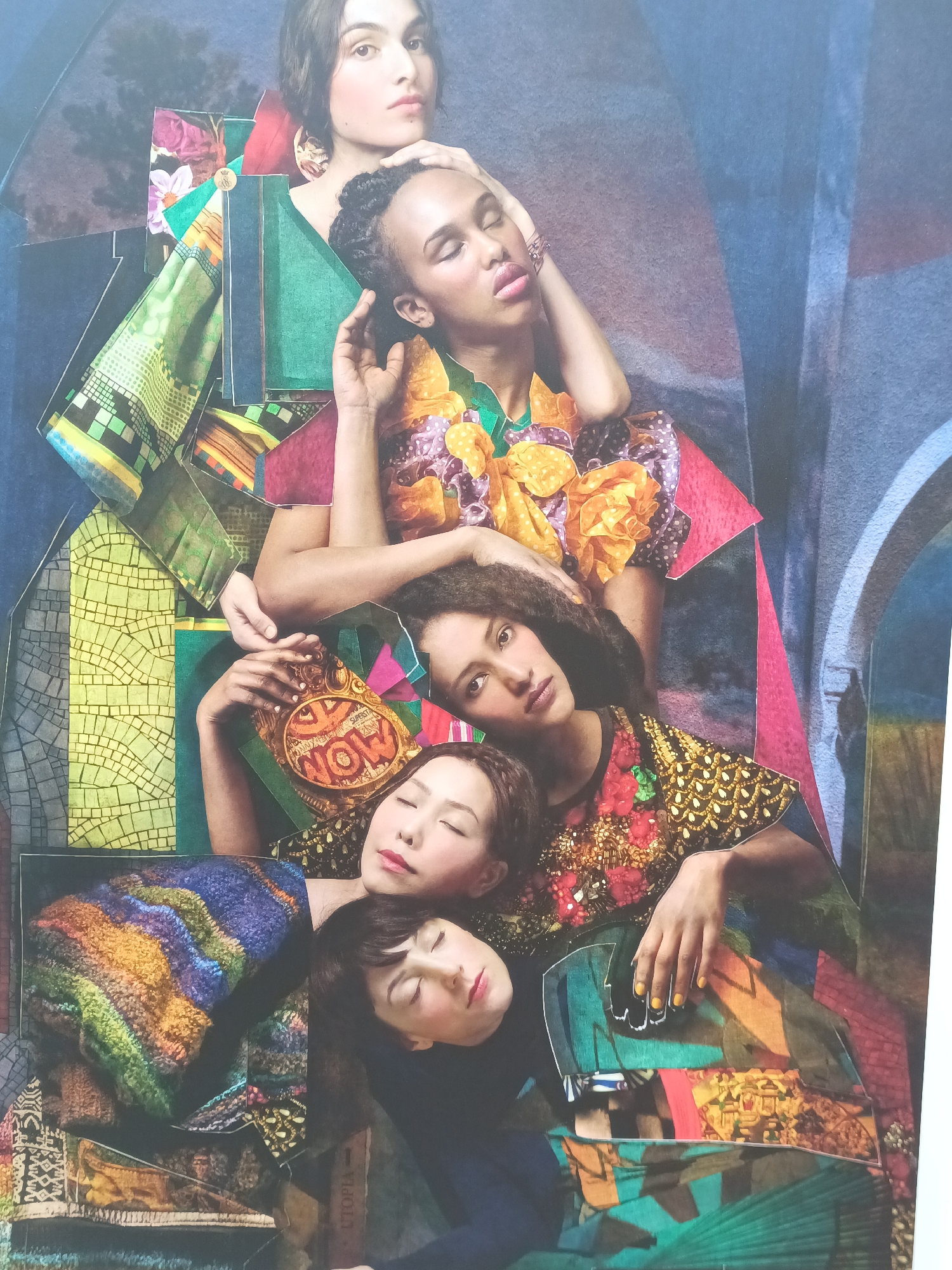 The image is a collage featuring four individuals posed in a tightly clustered arrangement. The arrangement appears to be staged. The backdrop is abstract and textured, with elements of blue and grey hues. There is no discernible depiction of the city of Houlgate, France. The focus of the collage is on the people and the vibrant, patterned fabrics that surround them.
The uppermost figure is a person with fair skin and dark hair, looking directly at the viewer. Below and slightly to the right is another person with darker skin and braided hair, eyes closed, with one hand resting on their head. To the left and below this figure is a third person with medium skin tone and dark hair, looking towards the viewer, with their head resting on the shoulder of the person above. Their body is adorned with a heavily embellished garment featuring floral motifs and gold beading. The fourth figure, at the bottom, is a person with fair skin and dark hair, eyes closed, with their head tilted upwards, adorned in a patterned garment.
The collage incorporates various fabric scraps with intricate patterns, geometric designs, and bold colors, creating a visually dynamic composition. Some of these fabrics overlap and frame the individuals. One of the figures holds a circular object with the word "NOW" visible. The overall impression is one of artistic presentation and emphasis on textural and color contrast.