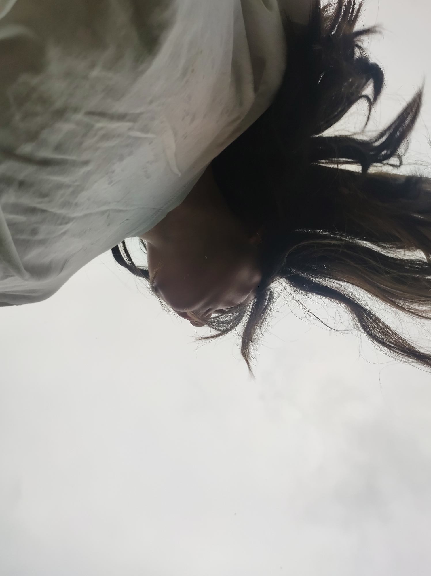 A woman lies on her back, looking up at the sky. Her brown hair is spread out around her head, and she is wearing a white shirt or blouse. The background is a cloudy, gray sky. There is no information available to confirm the location in the city of Фоки, Russia.
