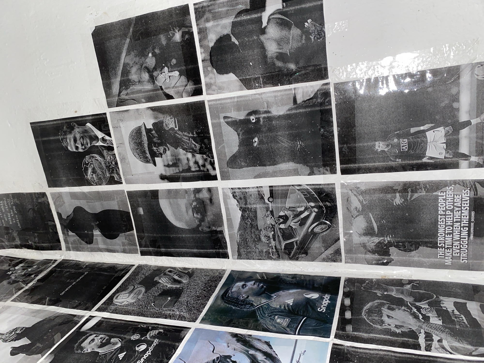 This media file displays a collection of black and white photographs adhered to a textured, off-white surface, likely a wall. The photographs are arranged in a grid-like fashion, with some overlapping and others taped.
The subjects are varied, featuring multiple individuals, predominantly male, in what appear to be sporting contexts, specifically football. One prominent image shows a footballer in a jersey with "AIG" and "Snapdragon" logos, possibly Cristiano Ronaldo, in action with a football. Another section shows a close-up of a footballer's face looking upwards. There are also images of a person in a military helmet, a black cat, a vintage car with occupants, and what appears to be a lunar surface or a large round object in the sky.
Some photographs include text. One image contains motivational text that reads: "THE STRONGEST PEOPLE MAKE TIME TO HELP OTHERS, EVEN WHEN THEY ARE STRUGGLING THEMSELVES. @MILLIONAIRE_DESIRES". Another has text that says: "OH HOW HE LOVES US". Additional text visible includes "Snapdragon", "AIG", "FA CUP", and what appears to be a name or signature in the bottom right corner of the frame.
The overall mood is a mix of sports enthusiasm, contemplation, and perhaps inspiration due to the motivational quotes. The setting appears to be an indoor space, given the way the photographs are displayed on a wall. The lighting seems to be artificial, illuminating the textured surface and the monochrome images. There are no clear indicators of time of day or weather conditions. The presence of football-related imagery and the mention of "FA CUP" suggest a connection to the sport, and the overall display could be a form of personal shrine, art installation, or motivational board. The location context of Jos, Nigeria, is provided, but there are no direct visual cues within the image itself to confirm this location.