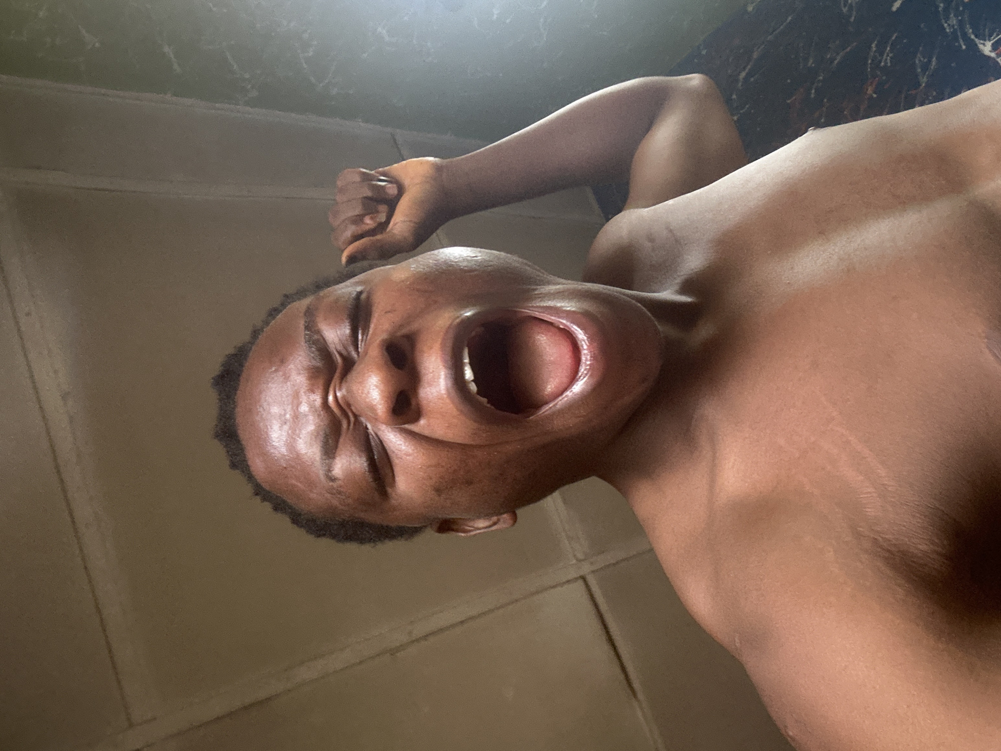 A shirtless person of African descent is screaming with a clenched fist raised. The location is indoors.