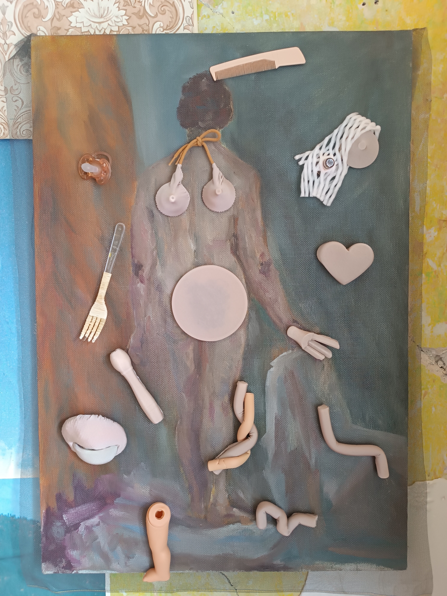 This image displays an artistic collage on a canvas depicting a semi-abstract, muted figure. Various objects, primarily made of light-colored material resembling clay or plastic, are arranged on the canvas and its surrounding textured background. These objects include a pacifier, a fork, a circular disc, a heart shape, a hand, a doll's leg, several abstract tube-like shapes, a comb, and a white object with intertwined white strands. The background incorporates elements of wallpaper and netting, suggesting an indoor setting. The specific location within the city of Yelets, Russia, is not discernible from the image content.