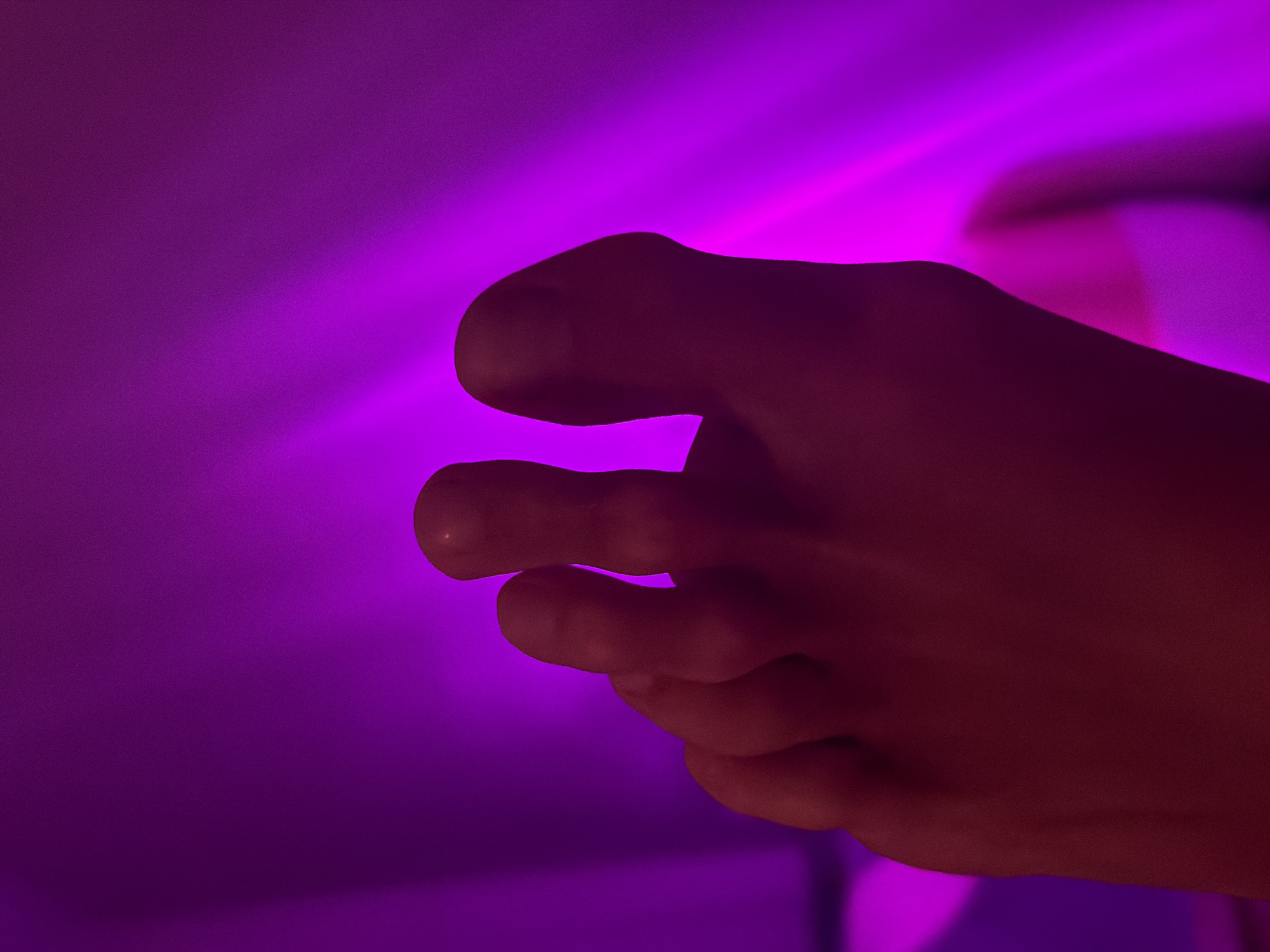 The image shows a close-up of a human foot illuminated with a purple light source. The foot is positioned against a blurred purple background. The lighting obscures details, but individual toes are discernible. There is no indication of the city of Saint Petersburg, Russia.