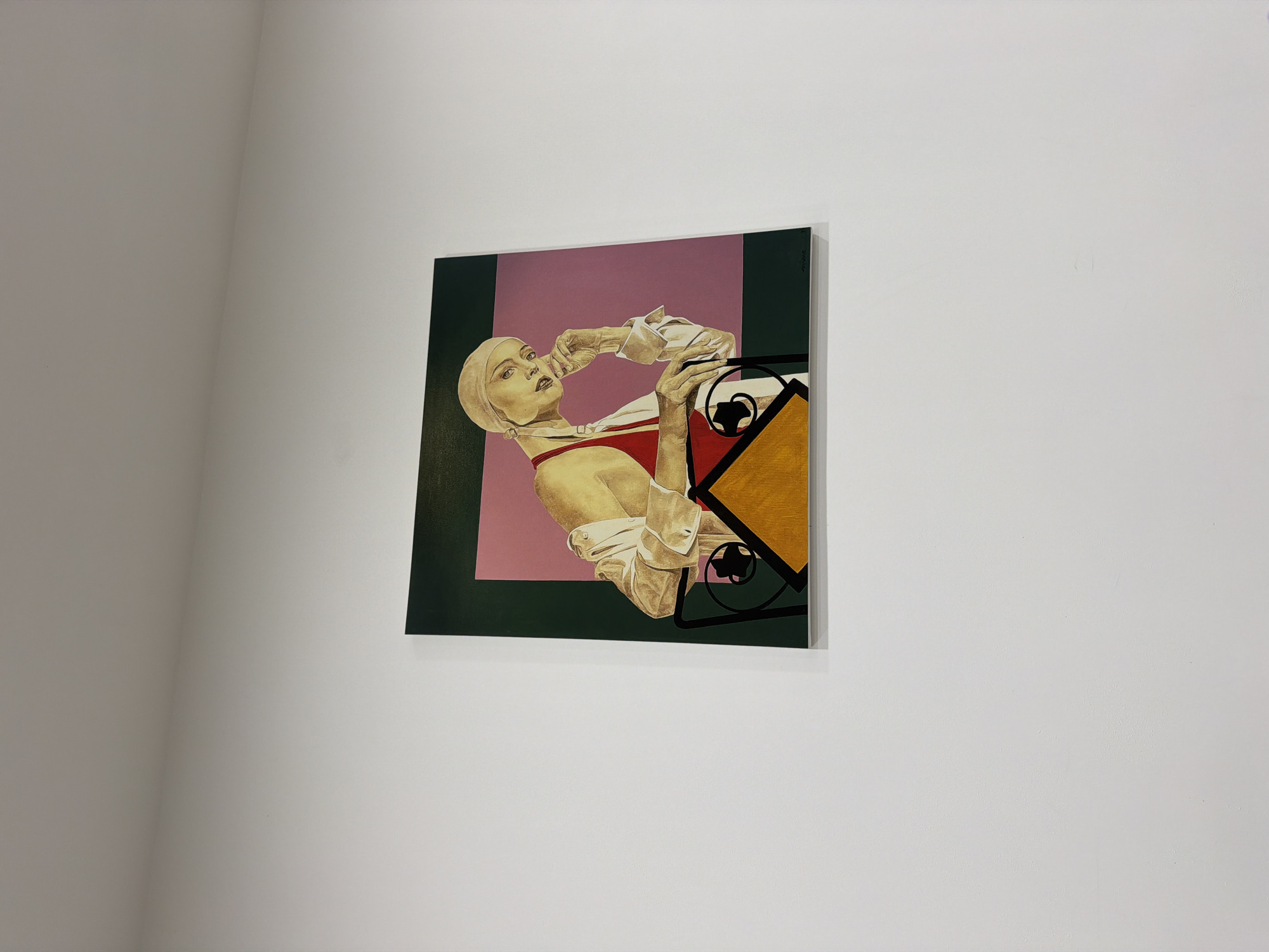 The image shows a painting of a woman, viewed from a slight angle, hanging on a white wall. The painting is predominantly square with a color scheme of green, pink, red, and gold. The woman in the painting is reclining, wearing a bathing cap and a red swimsuit, with a white collared shirt or jacket partially obscuring the view. Her hands are raised near her face. A geometric design incorporating black lines and a gold triangle is present in the lower right of the painting. The location is not ascertainable from the image, and there is no indication of the city of Sofia, Bulgaria.