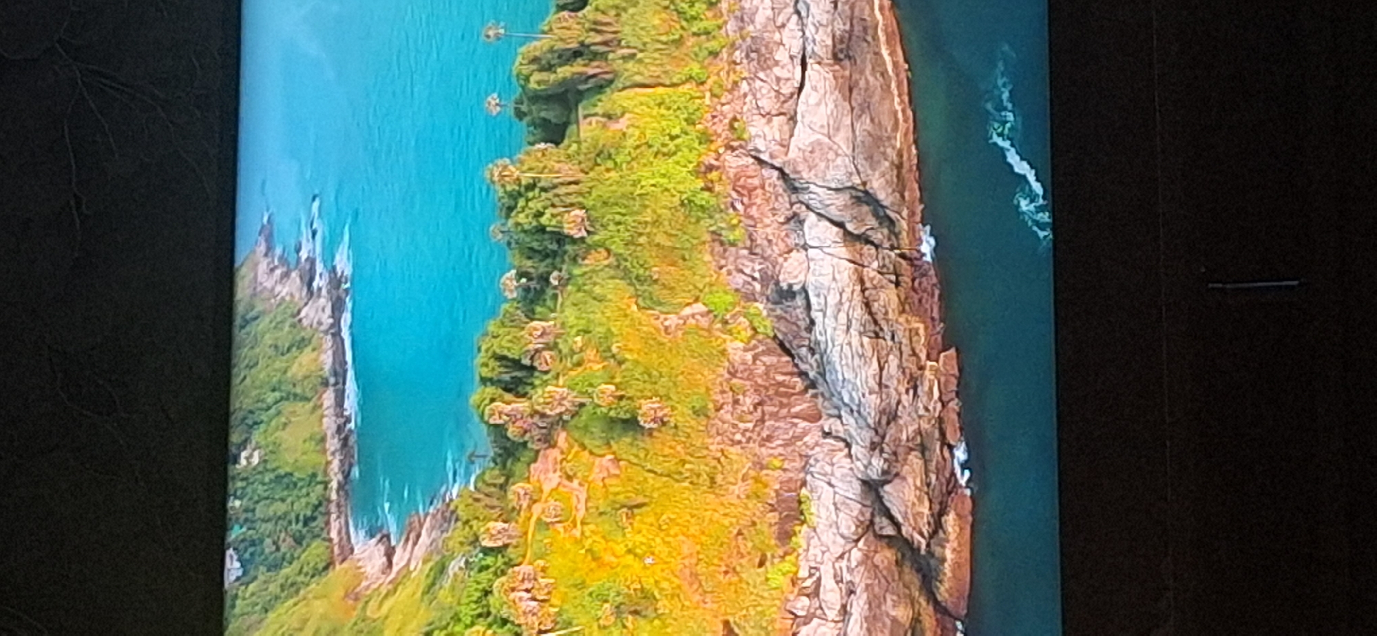 The image depicts a scenic coastal landscape. It features a rocky shoreline with crashing waves, lush green vegetation covering the cliffs, and a vibrant turquoise ocean. In the distance, a coastline extends with more greenery and hints of houses nestled amongst the trees. There are also palm trees scattered across the grassy slopes. The image has a slightly angled, aerial perspective, as if taken from a drone or a high vantage point.
The location is not in Bila Tserkva, Ukraine. Bila Tserkva is an inland city and does not have a coastline. This image is of a tropical or sub-tropical coastal region.